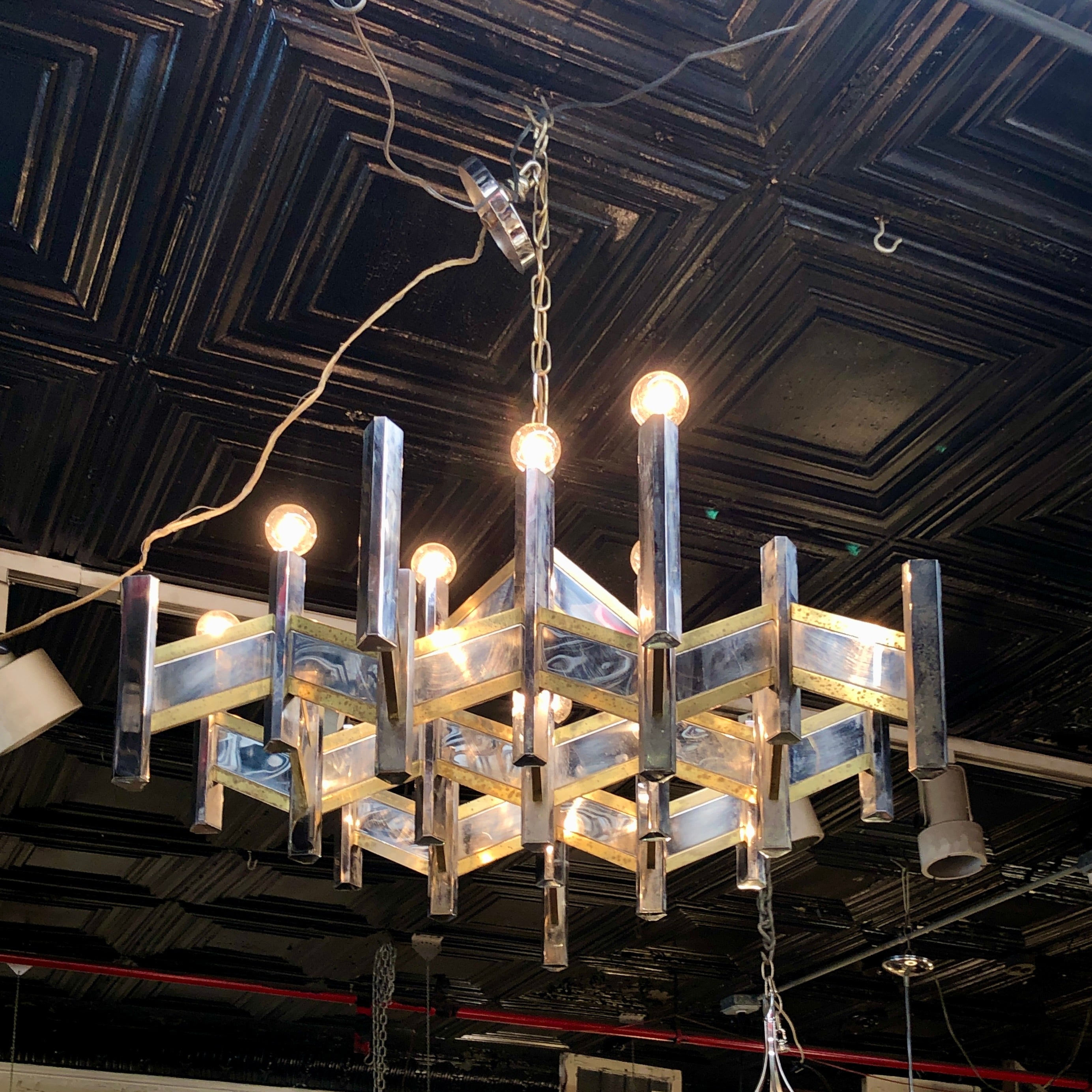 Lustre géométrique distinctif fabriqué en métal avec d'élégantes garnitures en laiton. Le design angulaire audacieux allie une structure moderniste à des détails métalliques chaleureux, créant ainsi un point focal saisissant pour les salles à