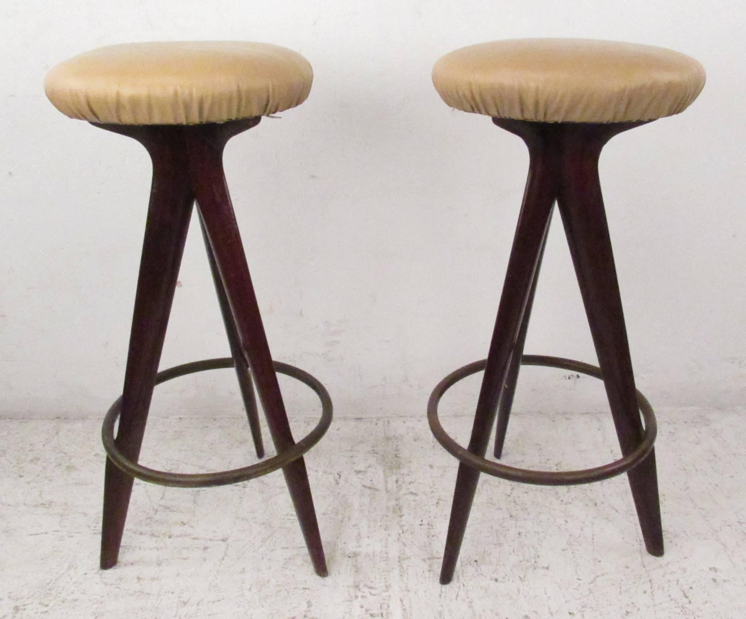 Stylish pair of three leg mahogany stools with brass foot rest and vinyl seats. Please confirm item location (NY or NJ) with dealer.
 