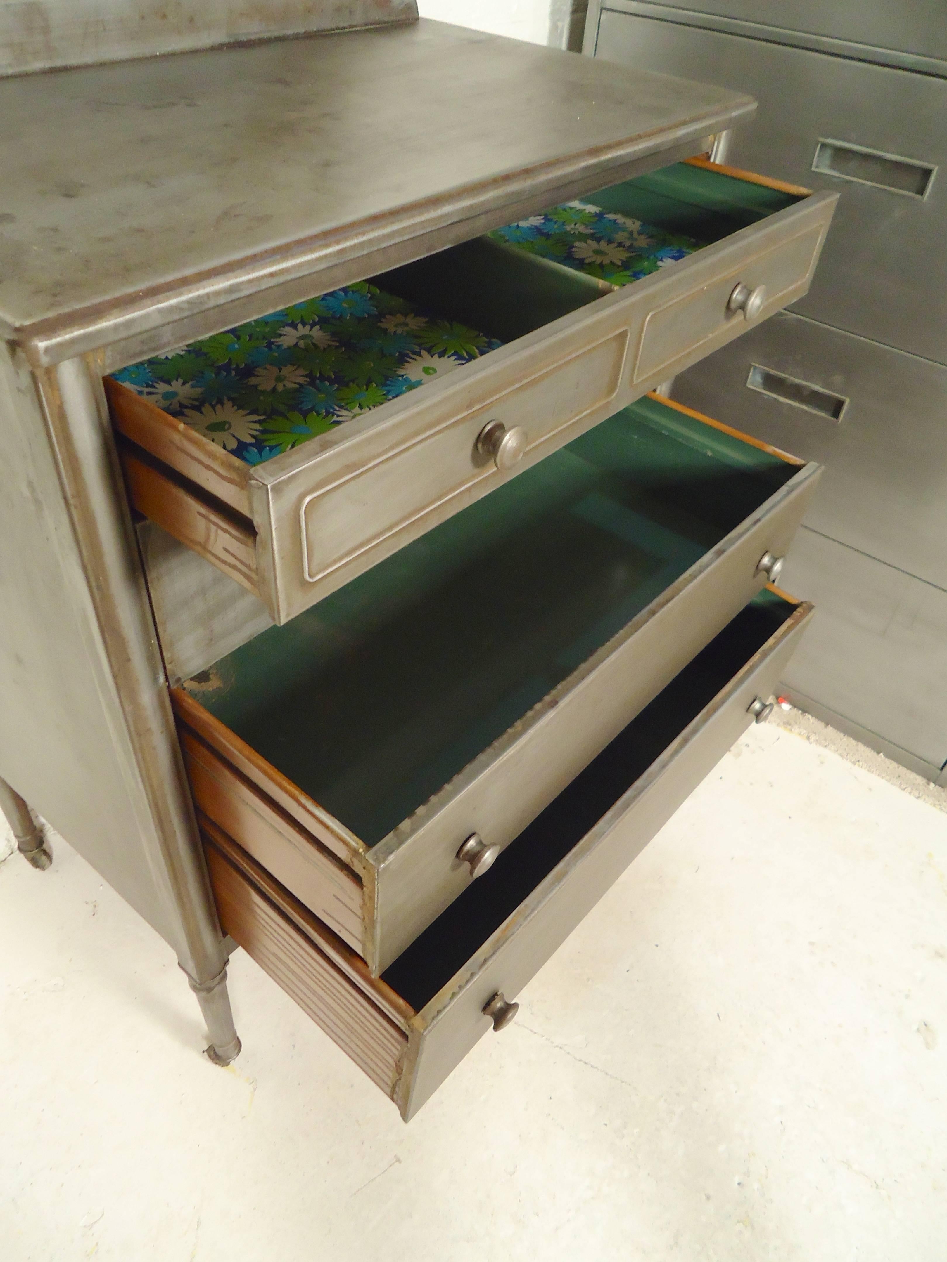 Unique metal dresser with mirror and pull-out table. Three wide dresser drawers, tilting mirror and small caster wheels. This dresser has been restored in a bare metal style finish, giving a distinct Industrial look.

Table height is 26