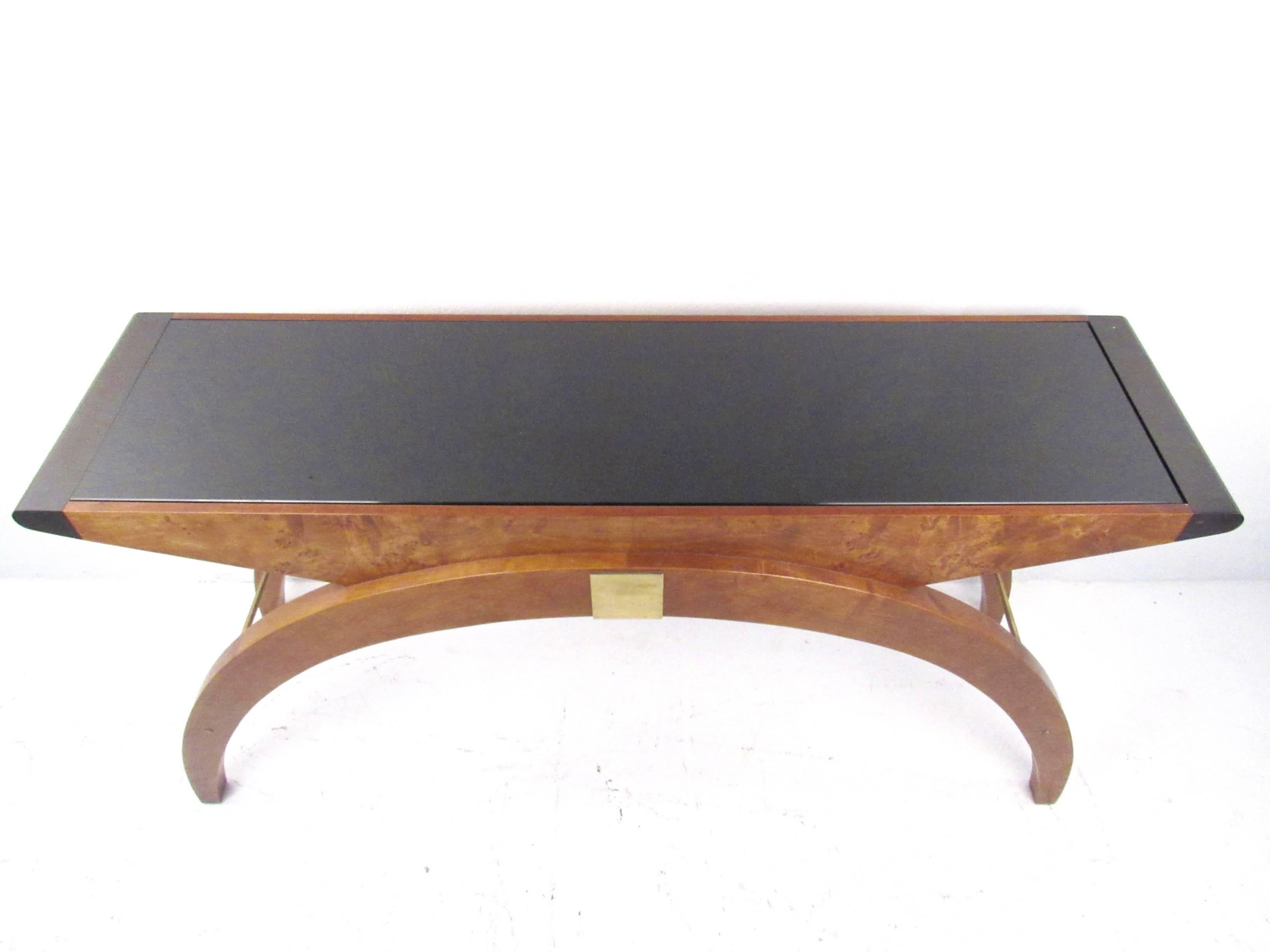 This beautiful sculpted console table boasts a unique mix of Art Deco style, modern simplicity and timeless elegance. Unique rounded legs, black formica style top, and brass trim add to the stylish Mid-Century design of the piece. Please confirm