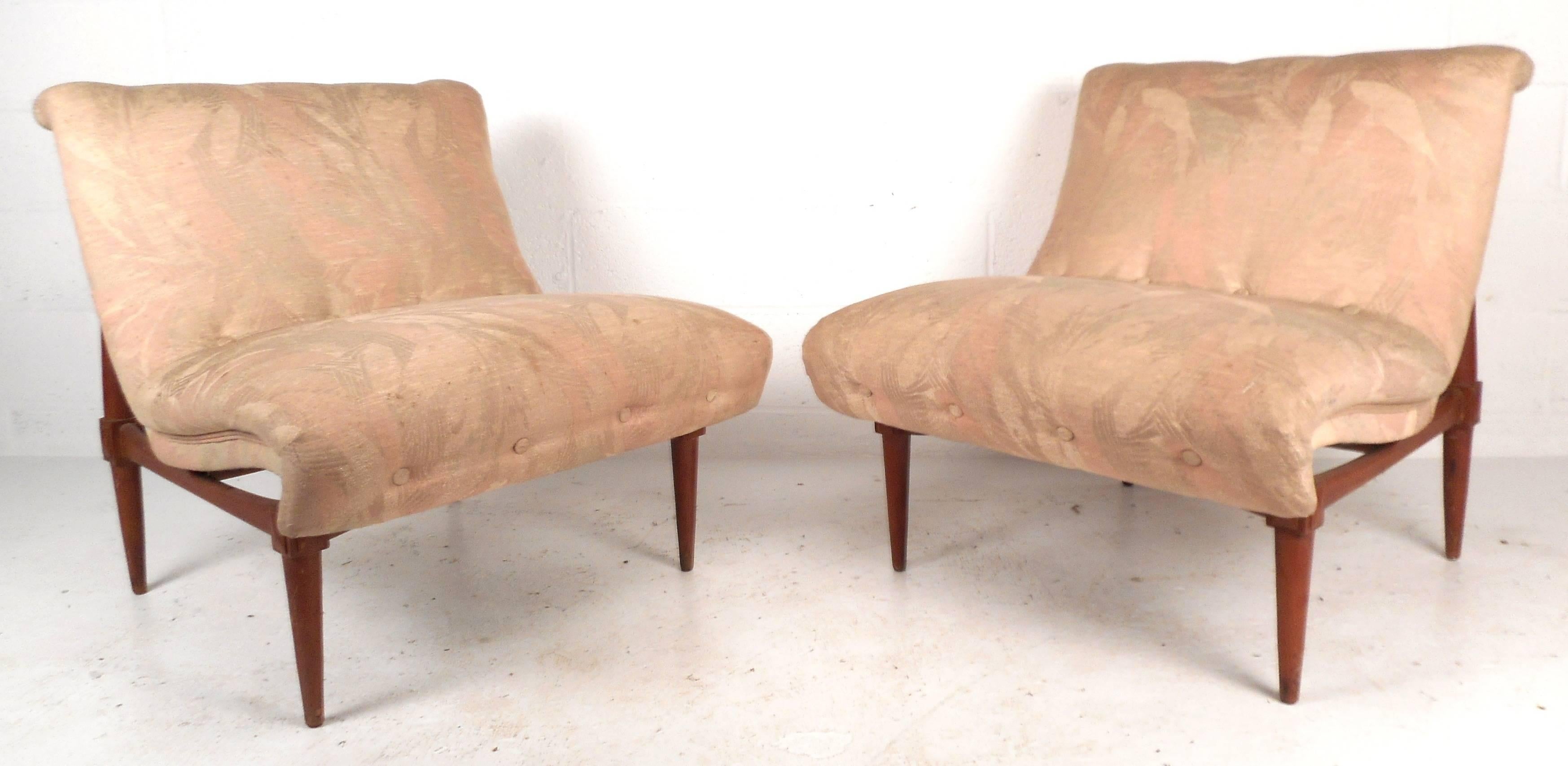 This beautiful pair of Mid-Century Modern slipper chairs features a unique sculpted walnut frame, vintage floral upholstery, and tapered legs. The impressive and comfortable wide seats and stylish armless design makes them a stylish addition to any