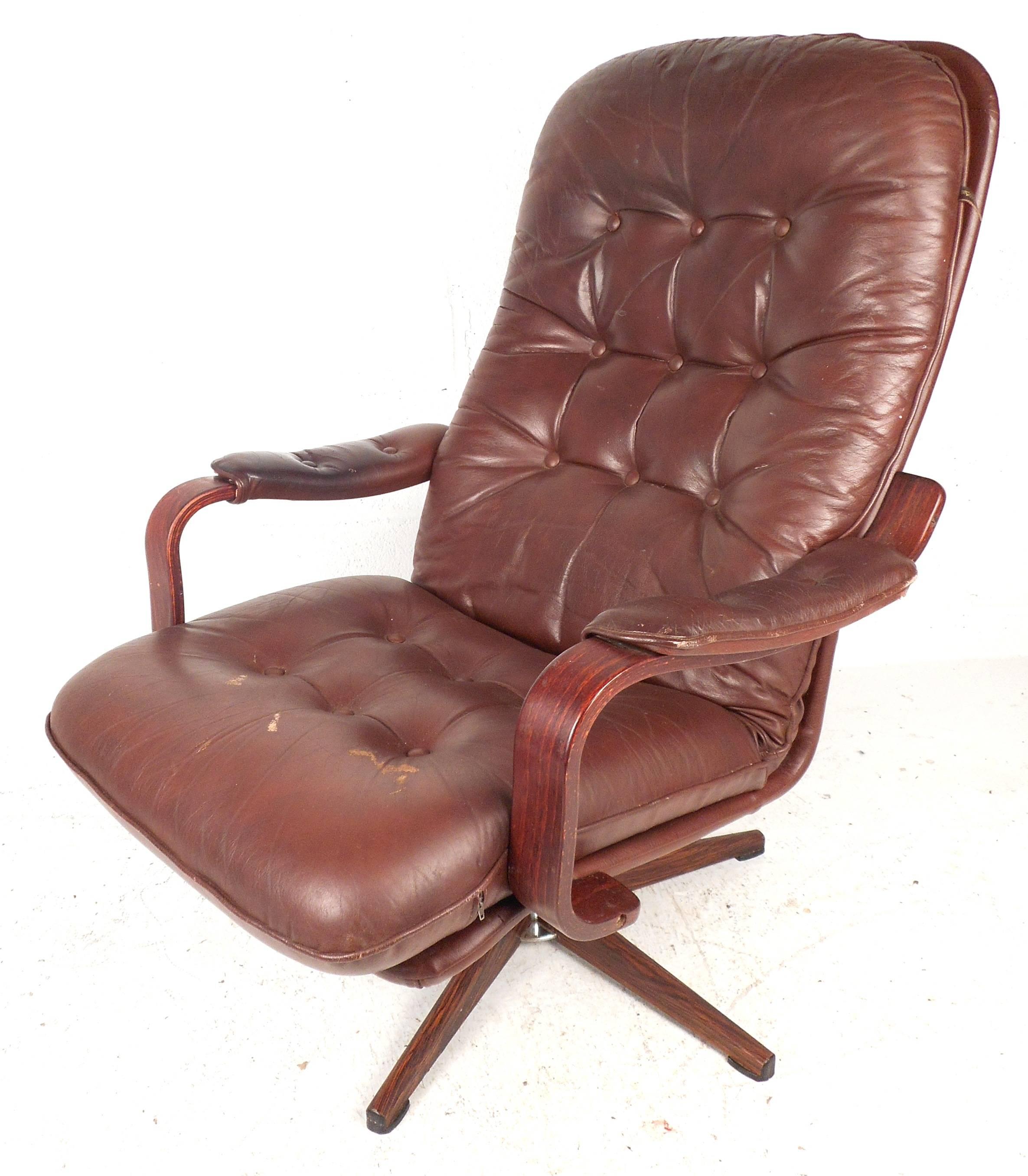 This gorgeous Mid-Century burgundy vinyl lounge chair and ottoman features tufted cushions, rosewood armrests and a swivel base. The comfortable and iconic design is labeled 