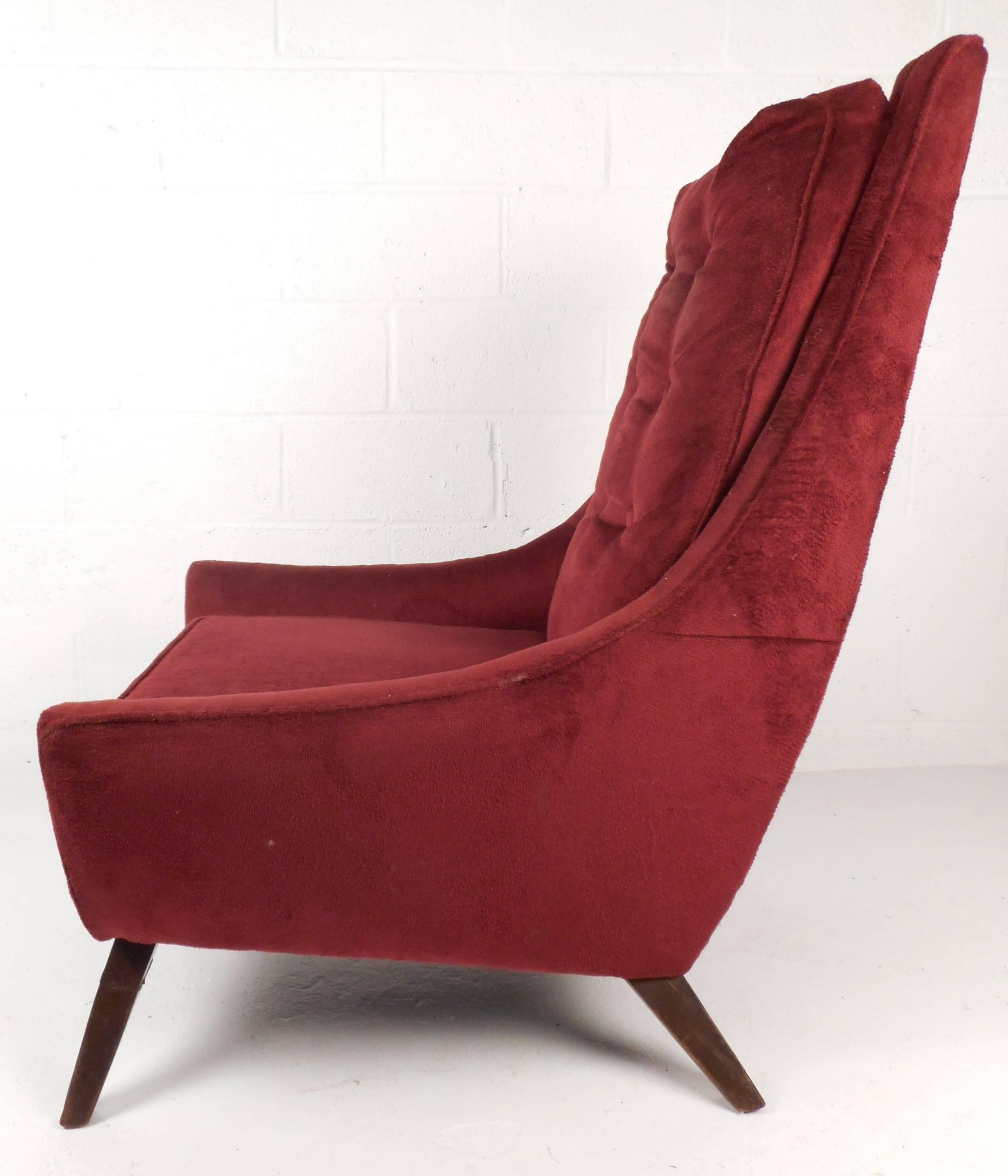 Stunning Mid-Century lounge chair features vintage crimson plush upholstery, solid sculpted walnut legs and tufted back rest. An overstuffed removable cushion and a high back rest ensure plenty of comfort. Sleek design with angled back legs adds