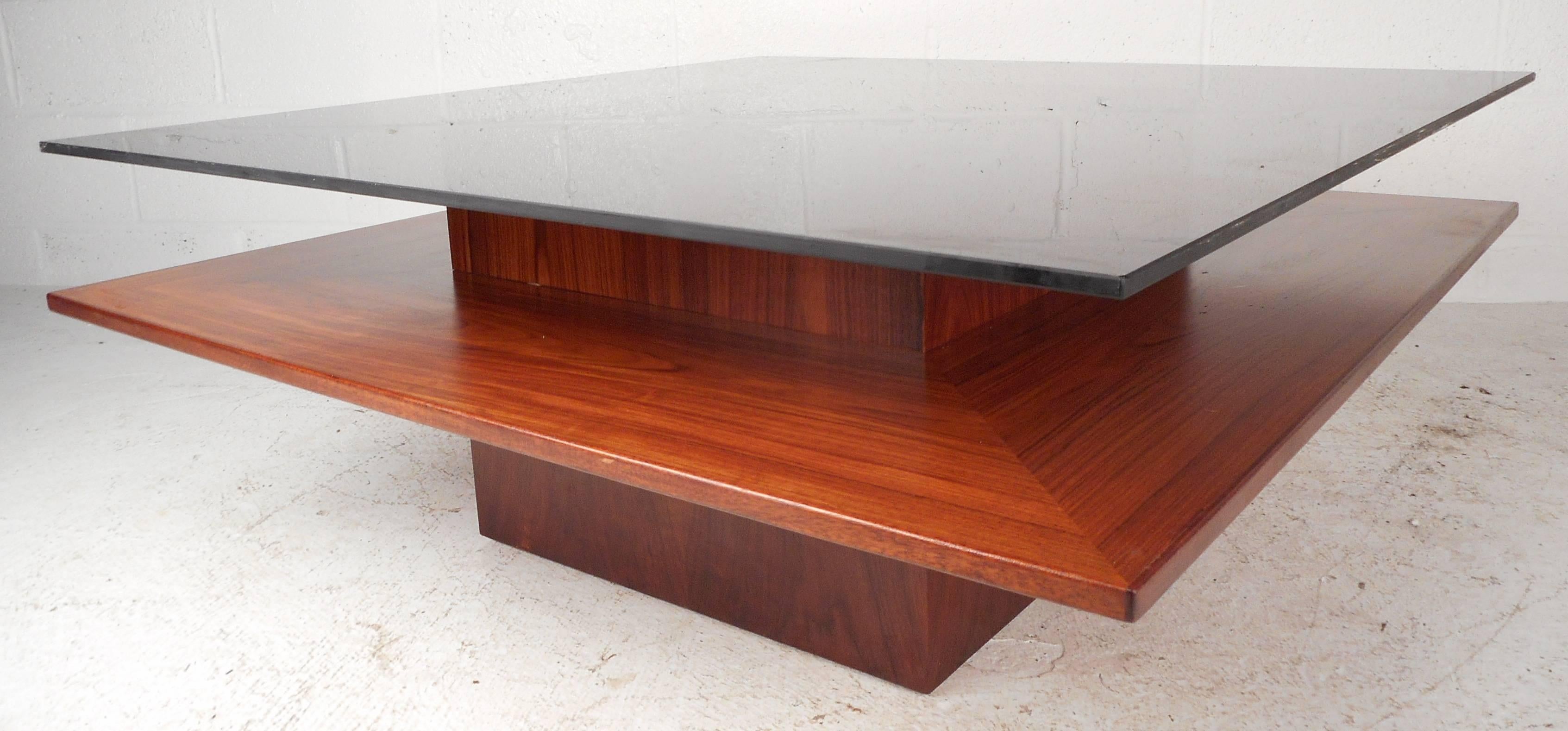 Elegant Mid-Century teak coffee table features a two-tier design with wood finish and smoked glass. A unique base provides style and sturdiness, while the smoked glass wonderfully compliments the vintage finish. Please confirm item location (NY or