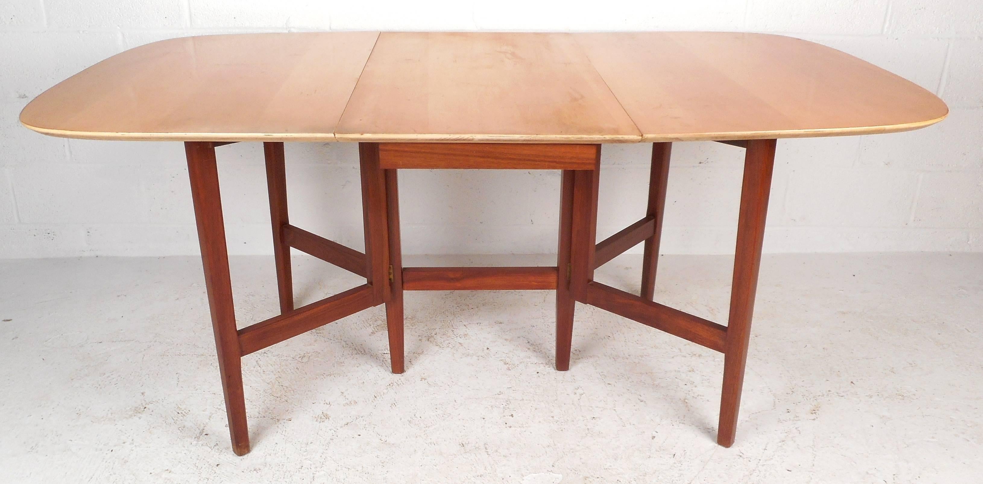 Stunning Mid-Century Modern drop-leaf dining table features solid walnut tapered legs and a vintage maple finished top. The stylish two-tone design and unique gate legs provide style and convenient storage in any setting. The dimensions when open