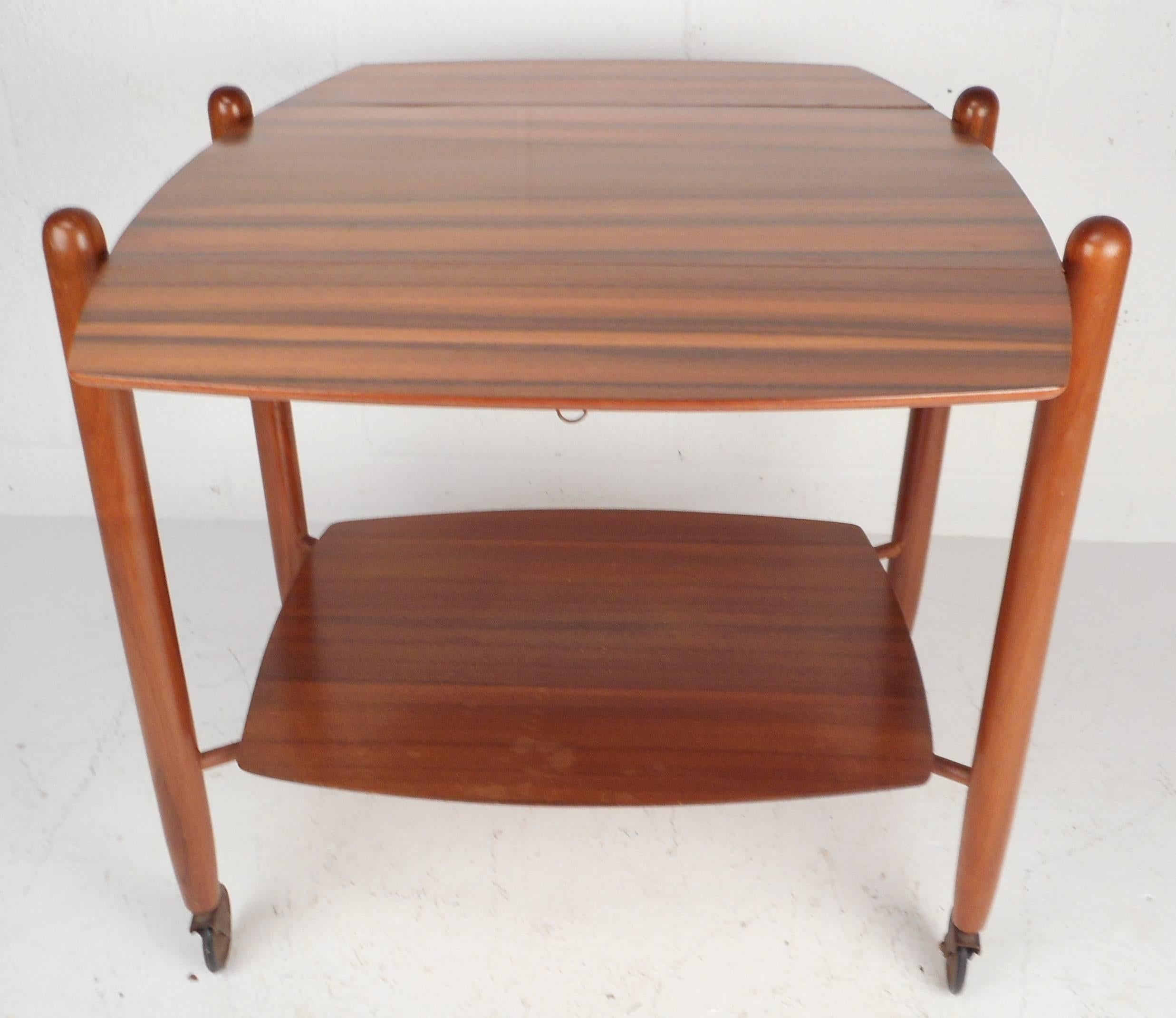 This elegant Mid-Century British bar cart is made of luxurious mahogany and features a versatile drop leaf design. The table is fixed now with no wheels, but can still accommodate wheels. When the leaves are open the dimensions are: 32