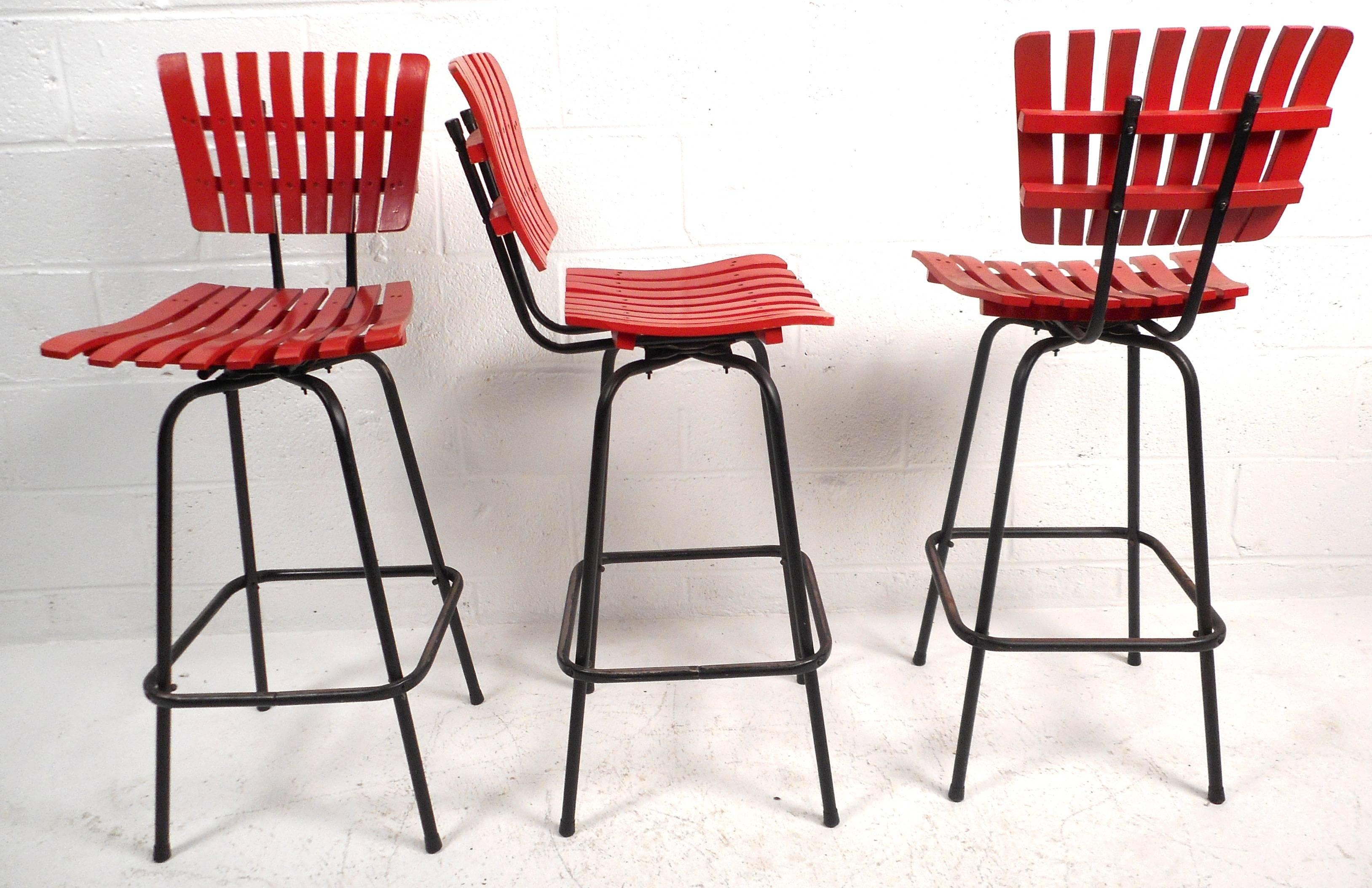 Lovely set of five vintage modern bar stools feature bright red slatted wood seats and backs, tubular iron bases, and a smooth swivel. The stylish design of Arthur Umanoff provides a unique look as well as comfort in any setting. Please confirm item