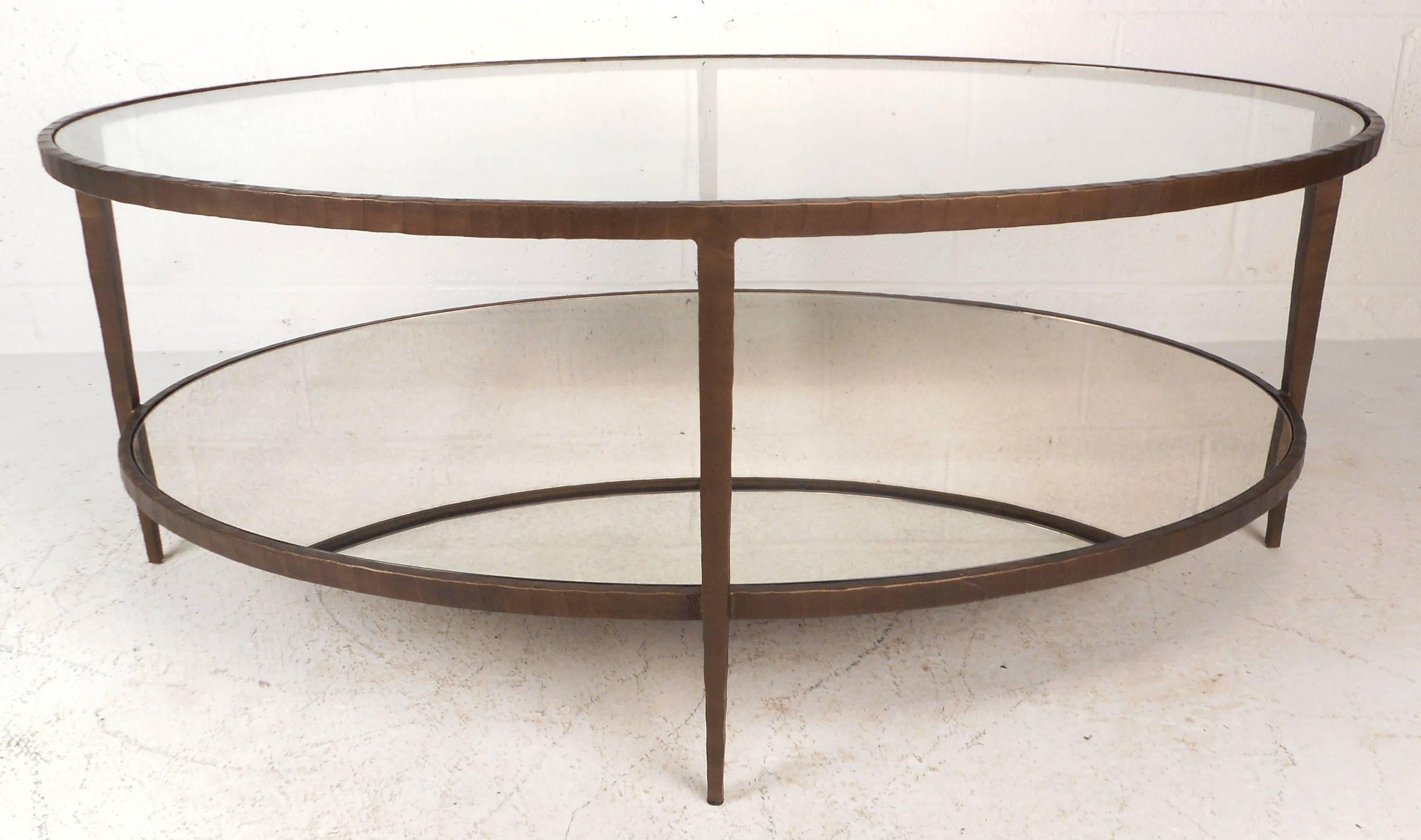 This vintage modern coffee table features a unique textured metal frame, a lower mirrored tier, and a thick glass top. The stylish oval floating tiers are supported by sturdy metal tapered legs. The elegant appearance is sure to compliment any