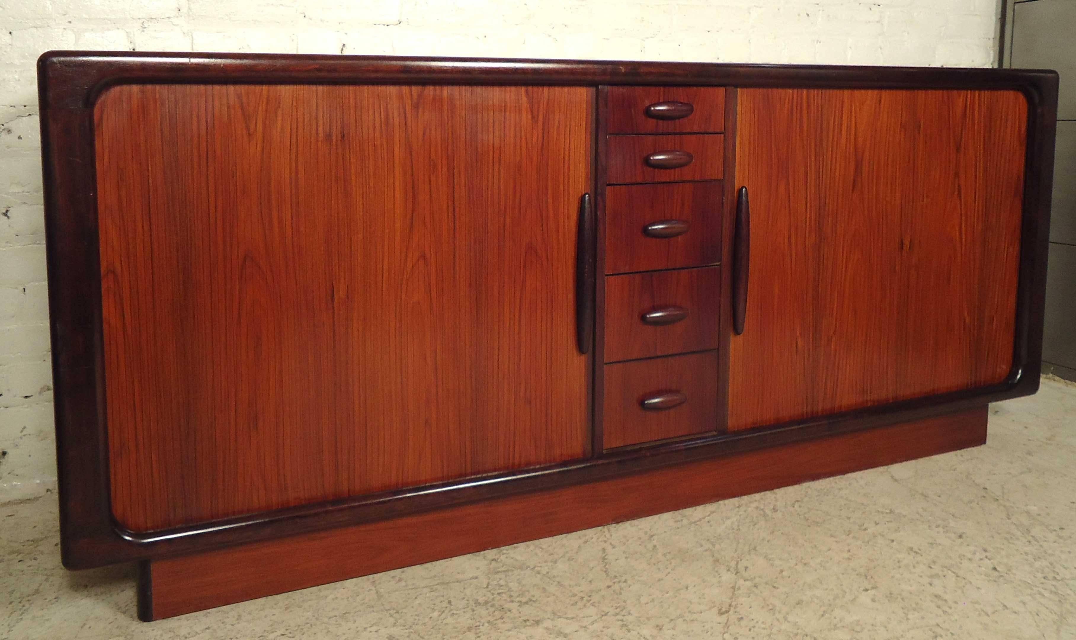 Unique vintage-modern server made of rich rosewood grain, features three large drawers, one shelving unit and a spacious compartment all behind a set of tambour doors. Including five smaller drawers in center with beautifully sculpted