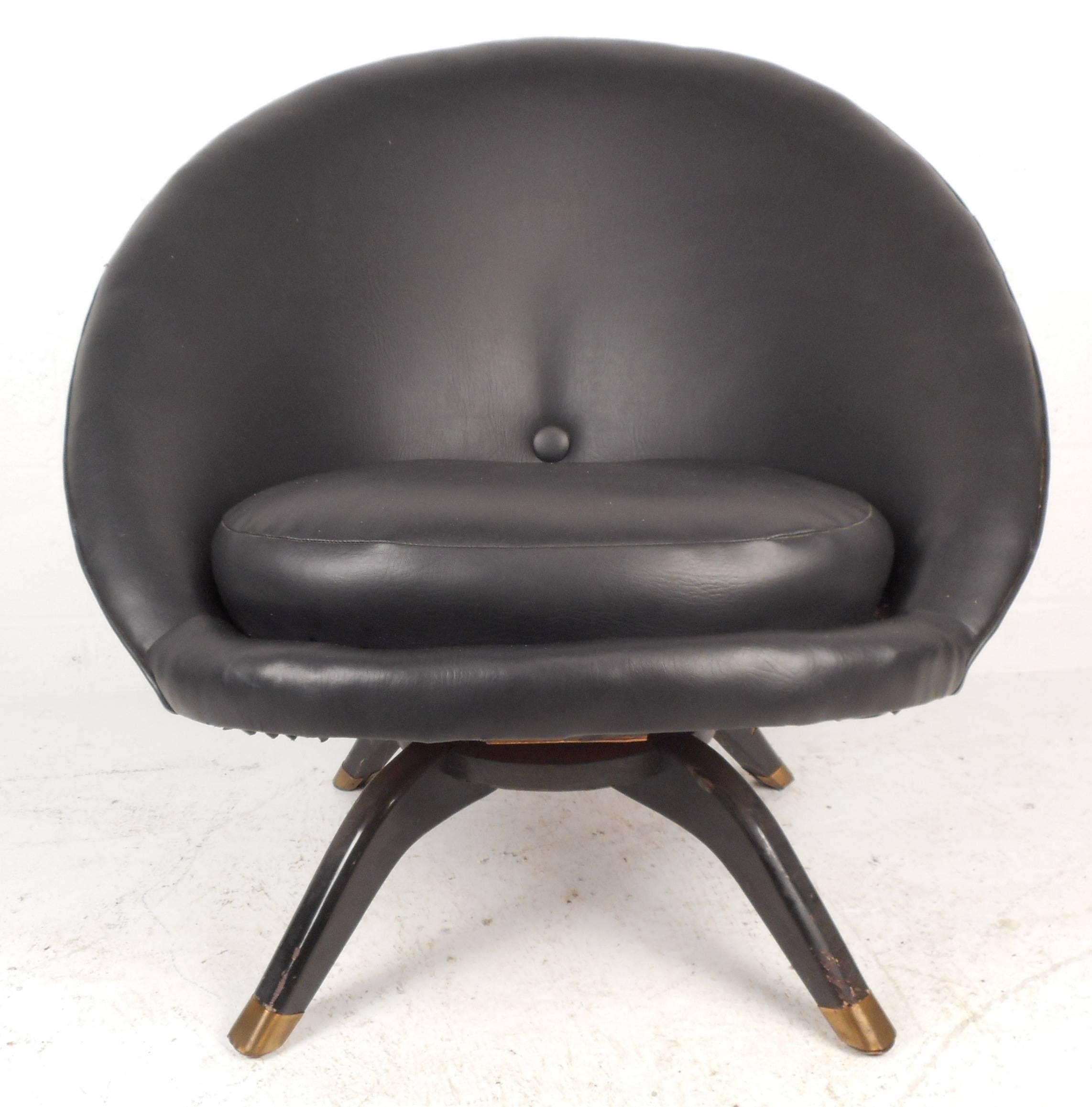 Lovely vintage modern pod chair features vinyl upholstery, swivel state, sculpted wood legs with brass capped feet, and a unique shapeld design. The thick cushion and wide seating are sure to add style and comfort in any modern interior. Please