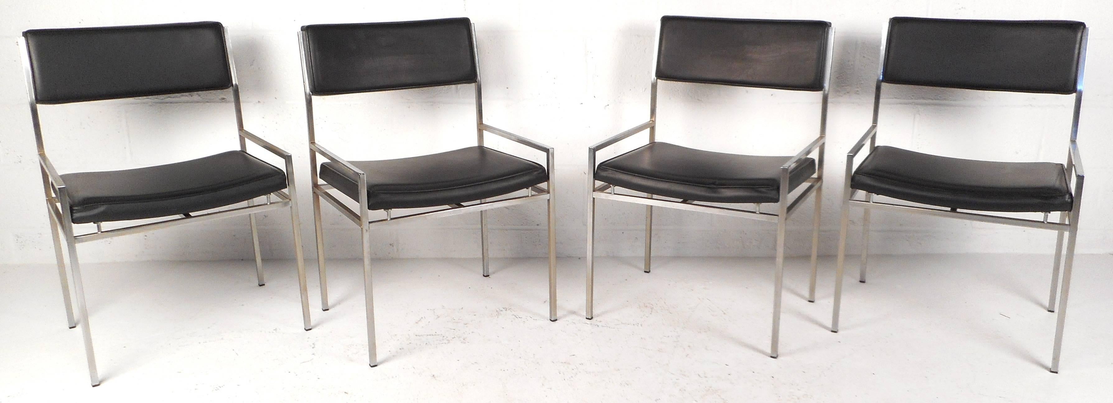 Stylish set of four vintage modern dining chairs feature unique low armrests, a sturdy chrome frame, and black vinyl upholstery. The sleek design has a slanted backrest and scooped seat ensuring optimal comfort in any seating arrangement. Please