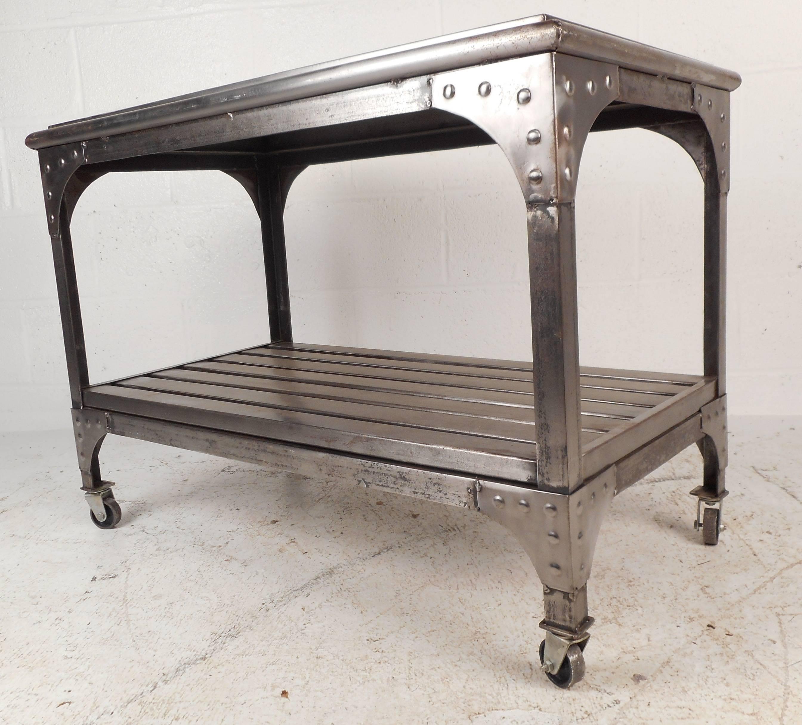 This vintage Industrial metal cart features two tiers for storage and a unique sculpted trim on the base. The bottom tier is slatted and the edges are secured with rivets showing quality craftsmanship. The sleek design has rounded edges on the top