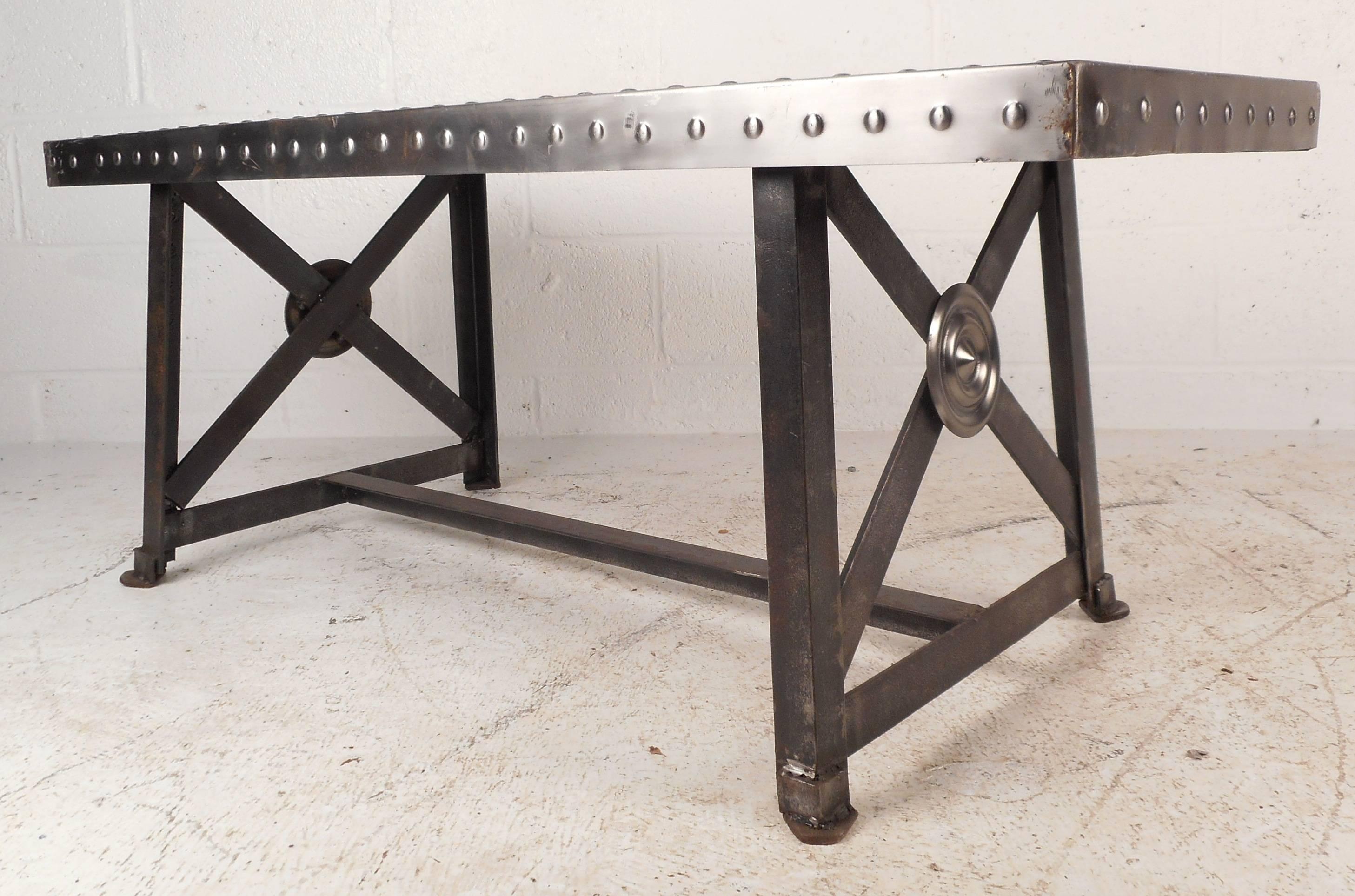 Beautiful vintage Industrial metal coffee table features a unique "X" design on the sides. The versatile piece can also be used as a bench, work table, or coffee table. Sleek design with rivets securing the edges and a heavy metal base