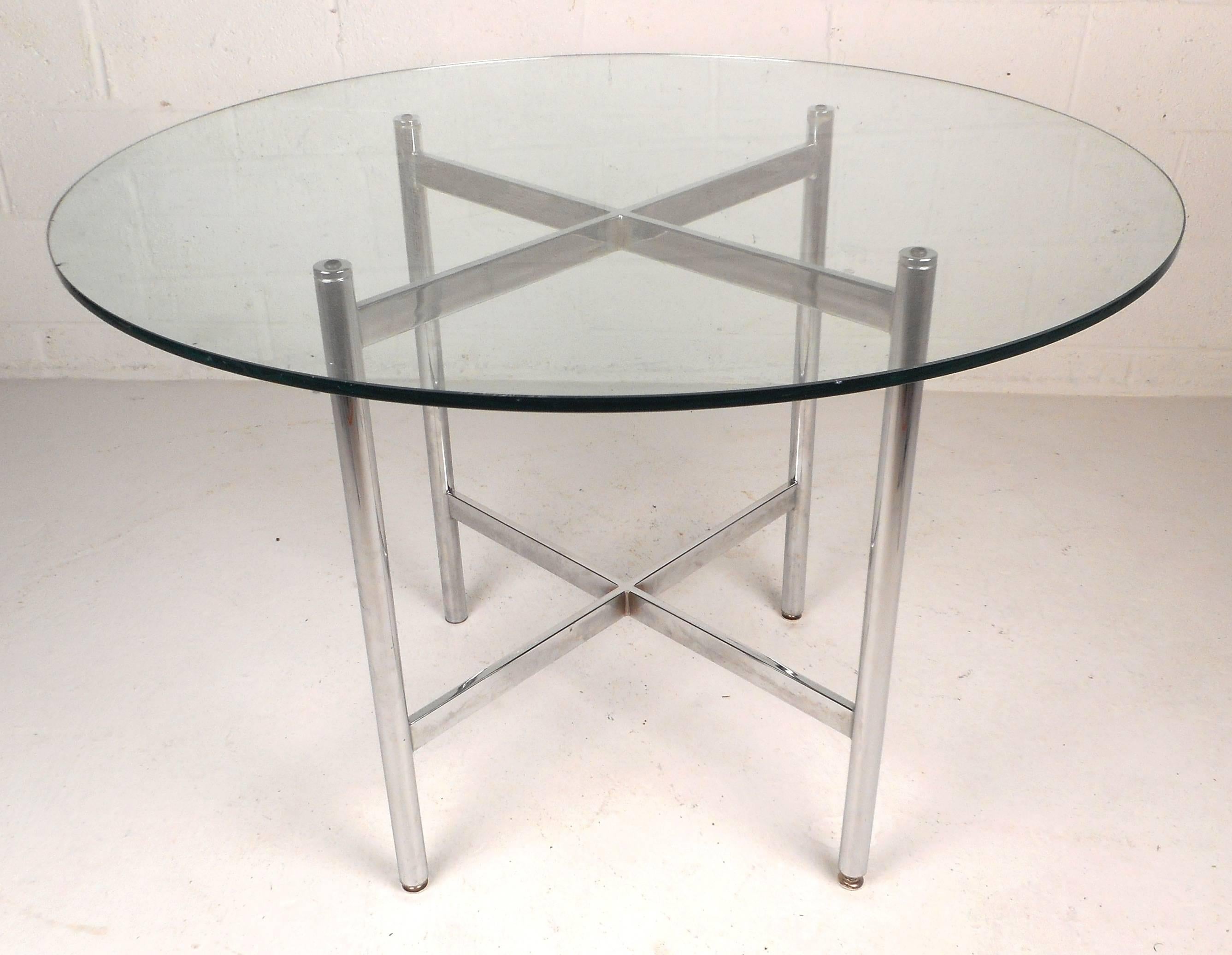 Stunning vintage modern dining set with a table and four-arm chairs. The dining table features a thick round glass top sitting on a heavy chrome base. Unique chrome stretchers form an 