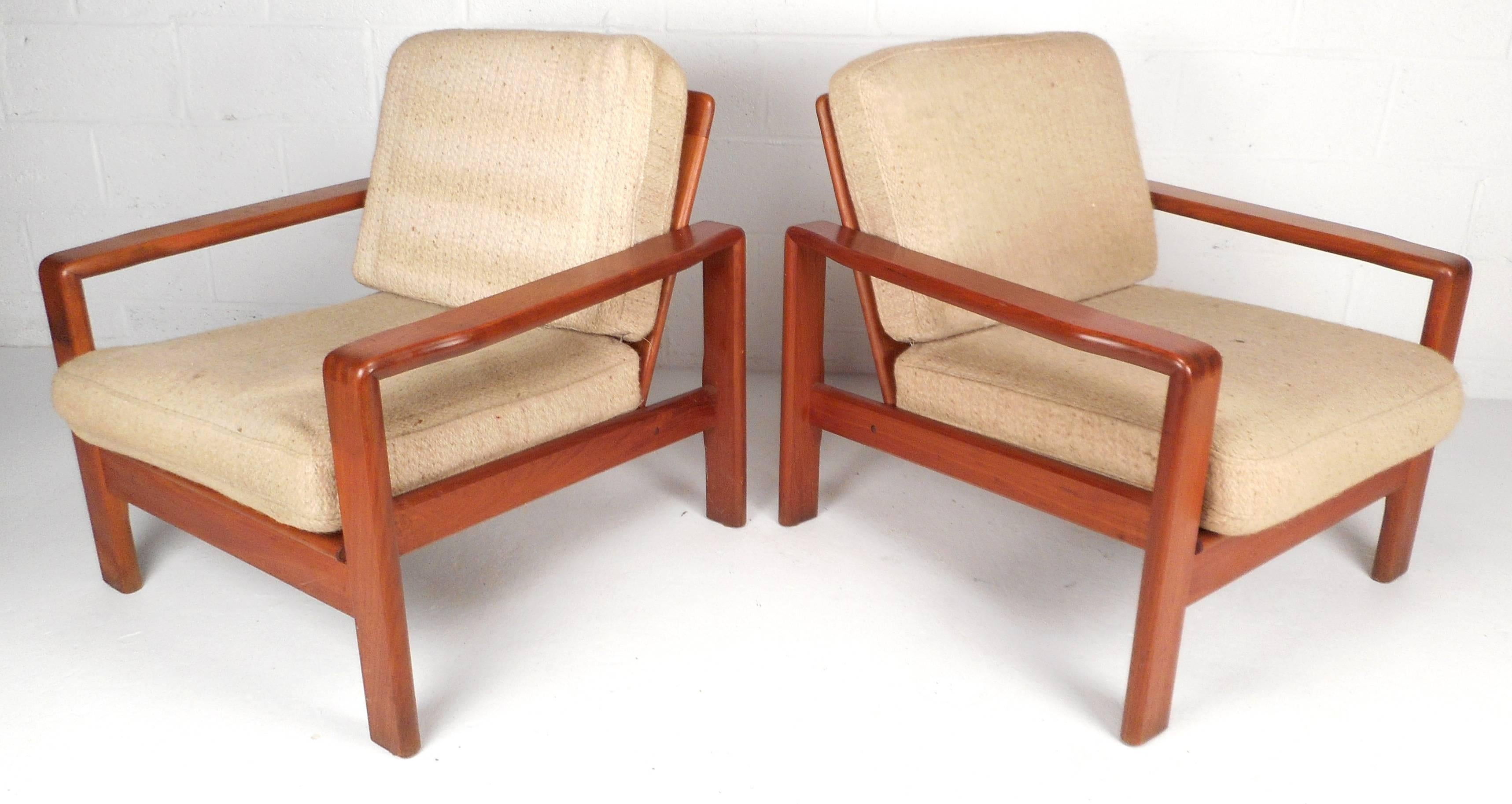 Stunning pair of Mid-Century Modern Danish teak lounge chairs feature solid teakwood frames and sculpted wide arm rests. Unique design has dovetail joints on the edge of the arm rests with a ladder backrest. Thick cushions and wide seating ensure