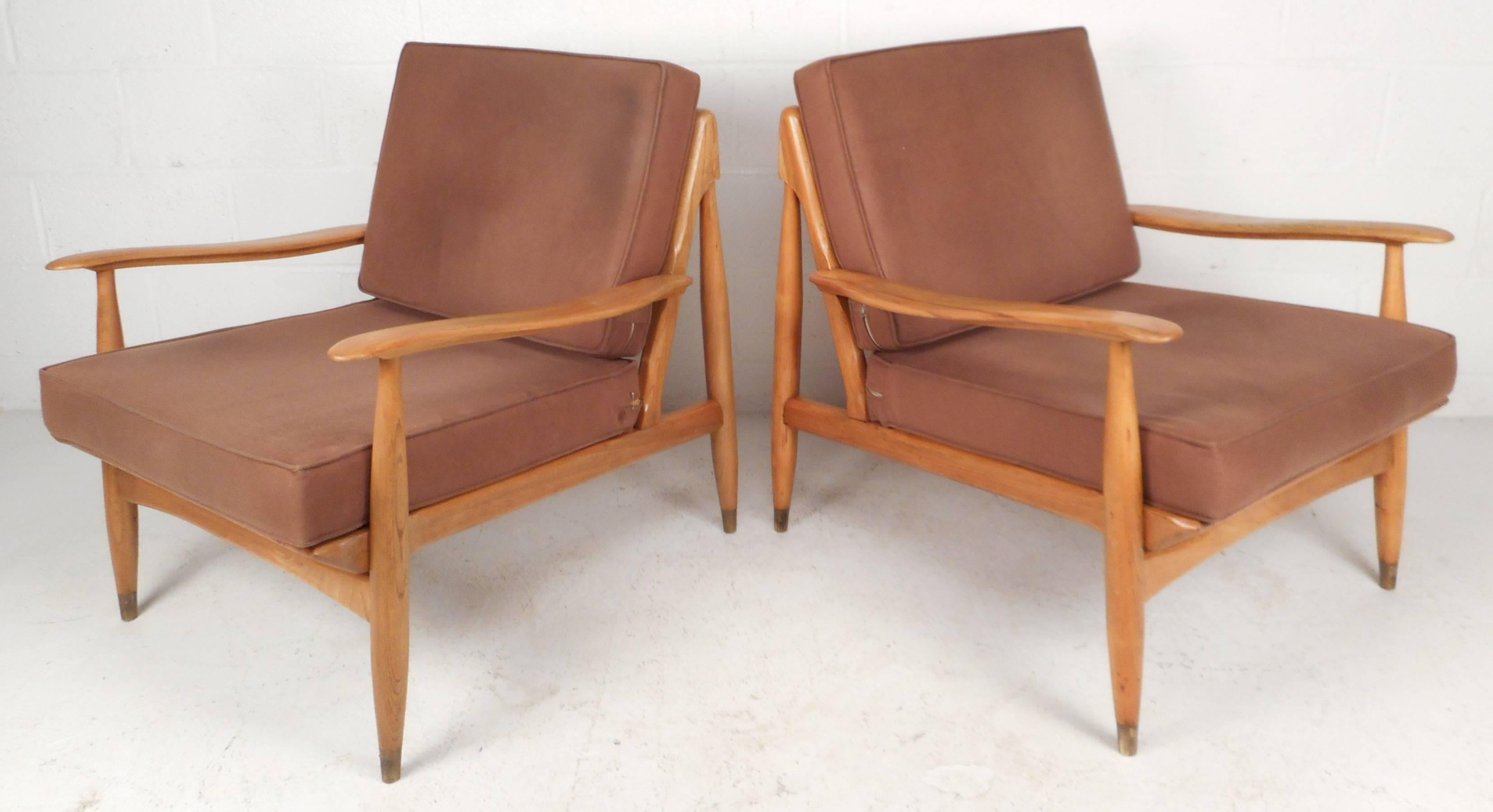 Beautiful pair of Mid-Century Modern lounge chairs feature a solid oak frame and sculpted armrests. Sleek design has tapered legs with brass caps on the feet. The thick cushions, wide seating, and plush upholstery ensure comfort without sacrificing