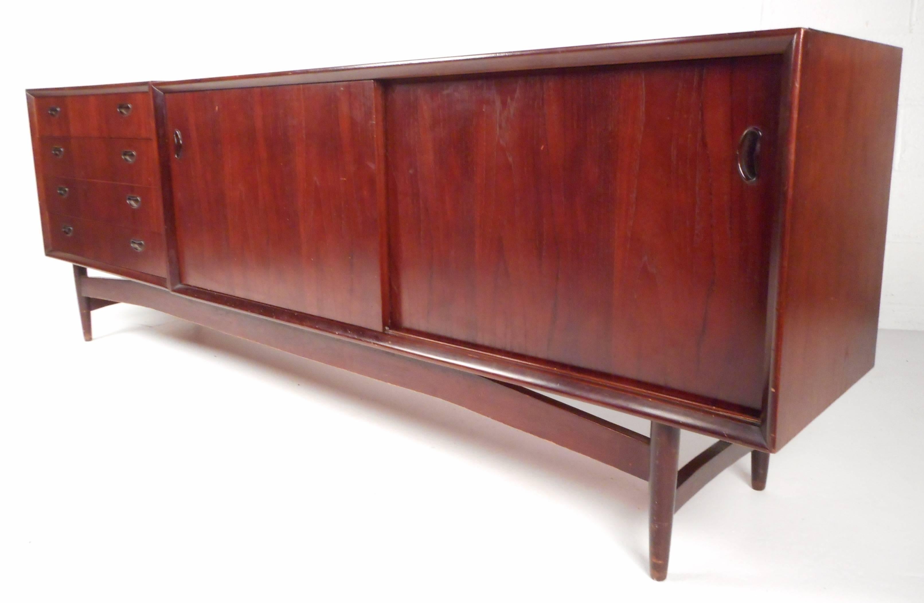 Impressive mid-century vintage sideboard features two separate pieces that sit comfortably on top of a sculpted base with tapered legs. Sleek design with unique carved pulls, a finished back, and gorgeous wood grain. Plenty of storage space in the