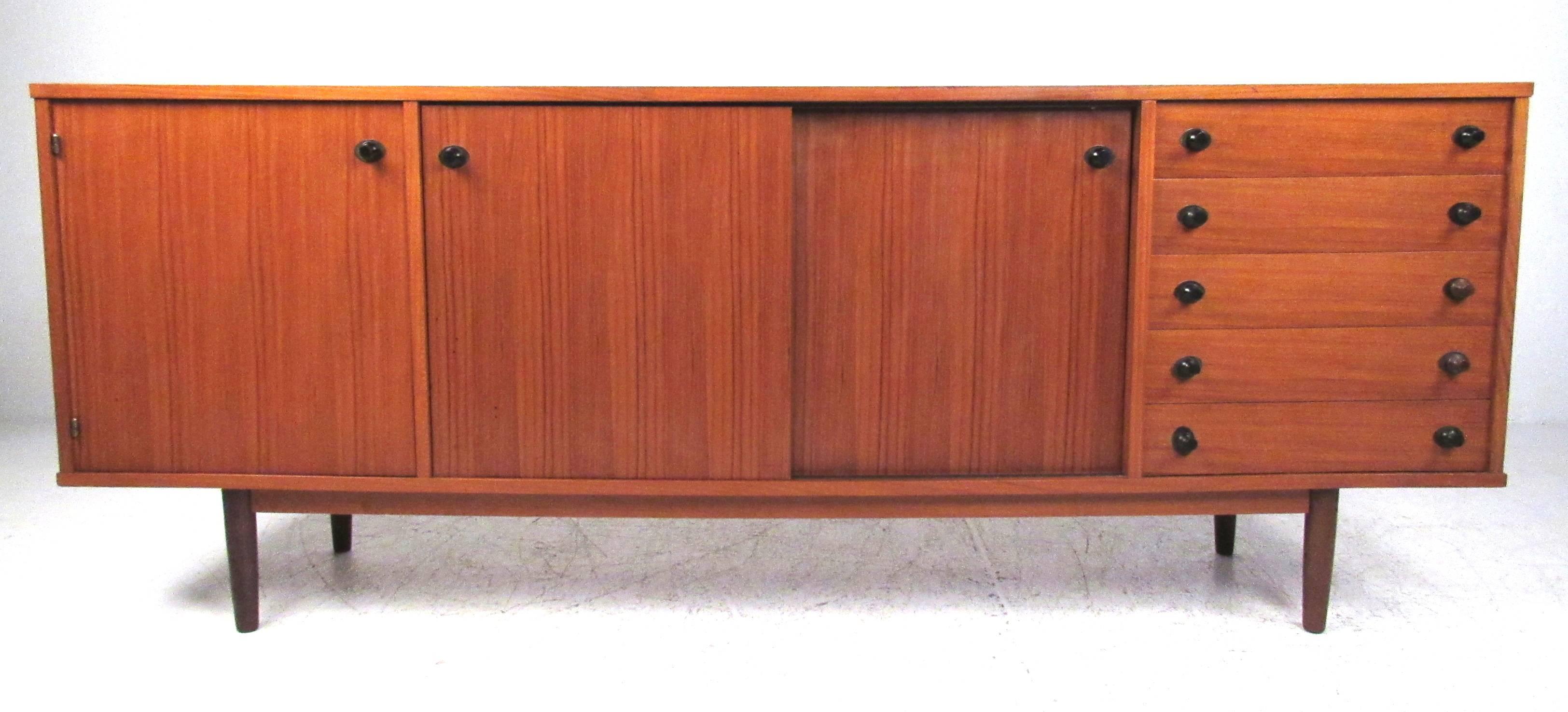 Nicely detailed five-drawer teak sideboard with two sliding door storage compartments and one hinged door. Sliding doors are reversible to a black painted finish and the two shelves are adjustable. Finished back is teak also. Please confirm item