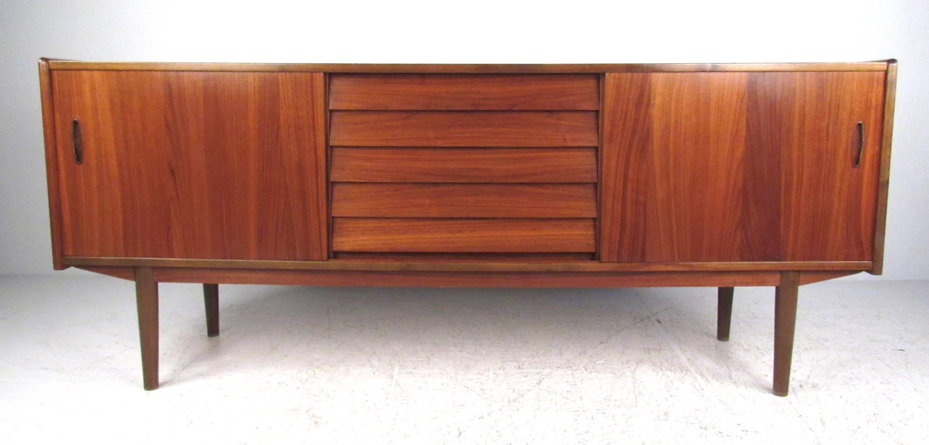 Vintage teak sideboard featuring five drawers and two sliding doors with adjustable shelves. Elegant Swedish modern sideboard features storage for dining room or use as a mid-century style TV or office console. Stylish teak finish adds vintage