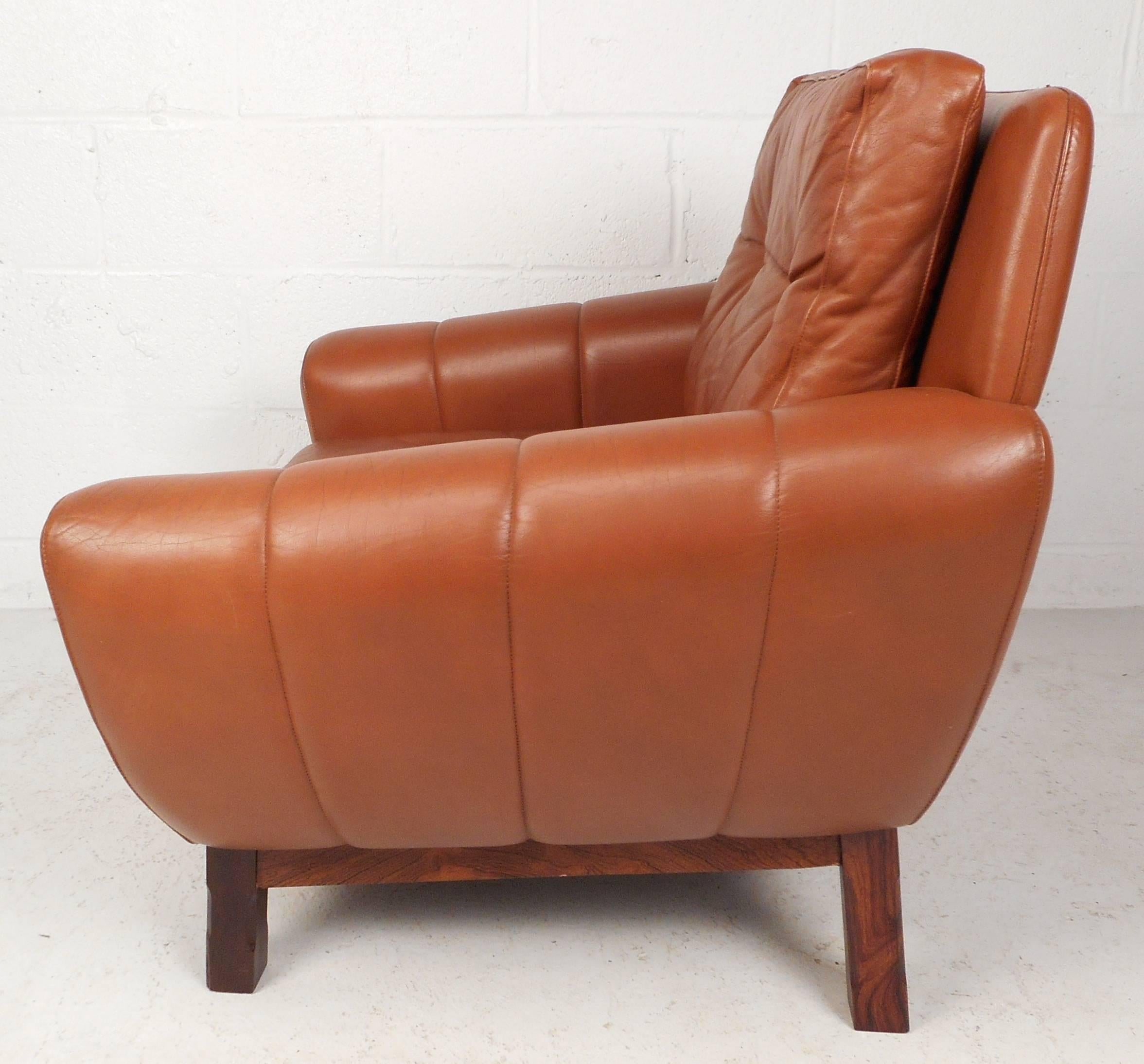 Beautiful vintage modern Danish lounge chair upholstered in orange leather. Comfortable design features wide seating, large armrests and thick cushions. The unique rosewood base and the stylish tufted backrest make it the perfect addition to any