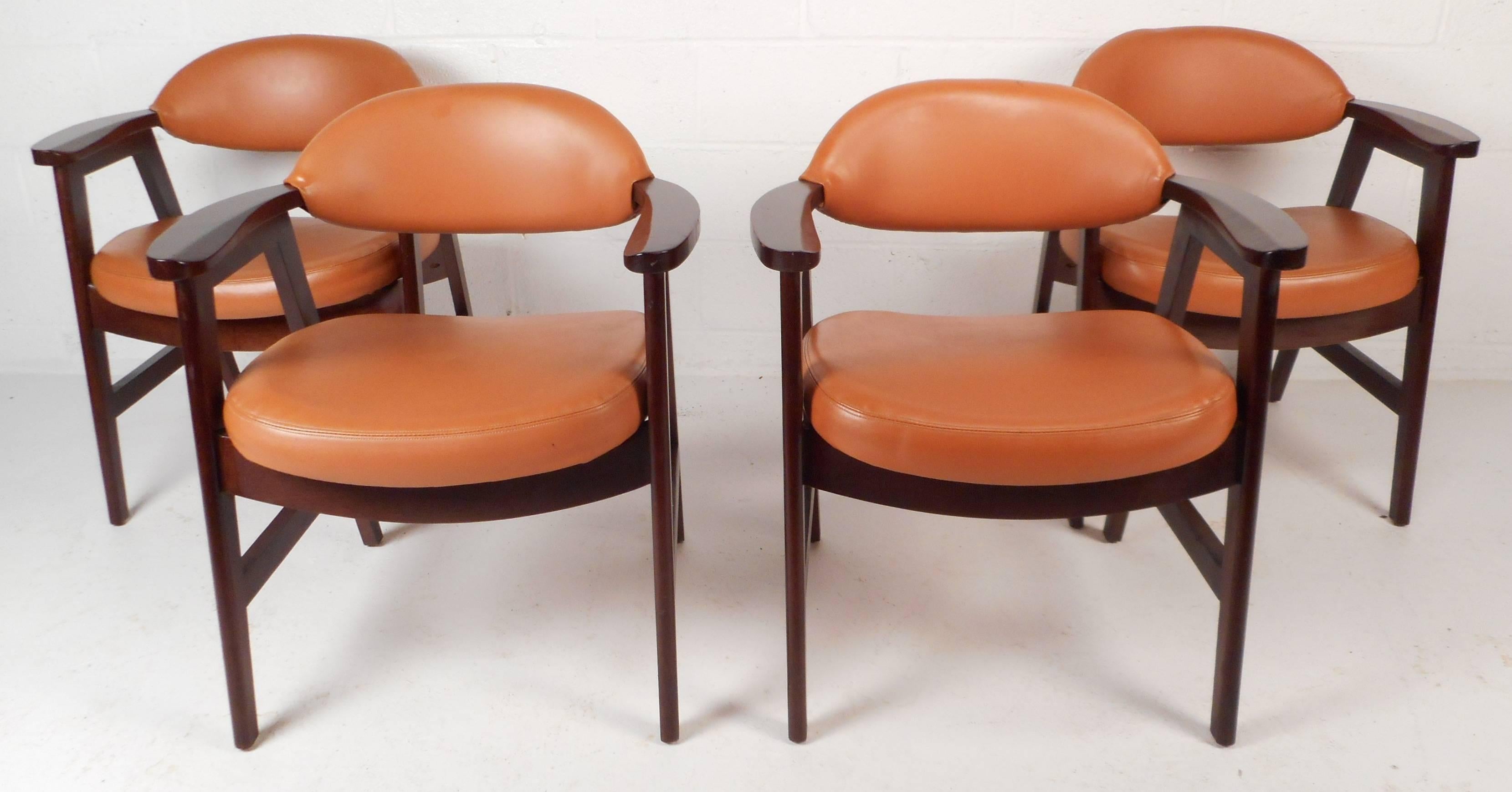 This stunning set of four vintage modern dining chairs feature a solid walnut frame with unique beveled armrests. Sleek design with thick cushions and beautiful bright orange vinyl covering. The slanted legs and barrel backrest offer style and