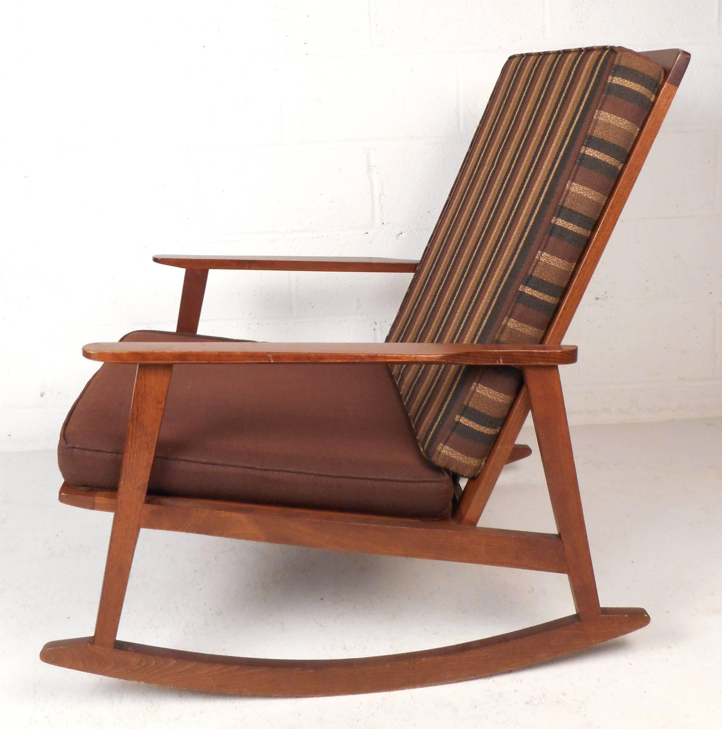 Lovely Mid-Century Modern rocking chair features a vintage walnut finish and sculpted arm rests. Sleek design with a smooth rocking motion. The unique high spindle backrest, vintage upholstery, and thick cushions are sure to compliment any modern