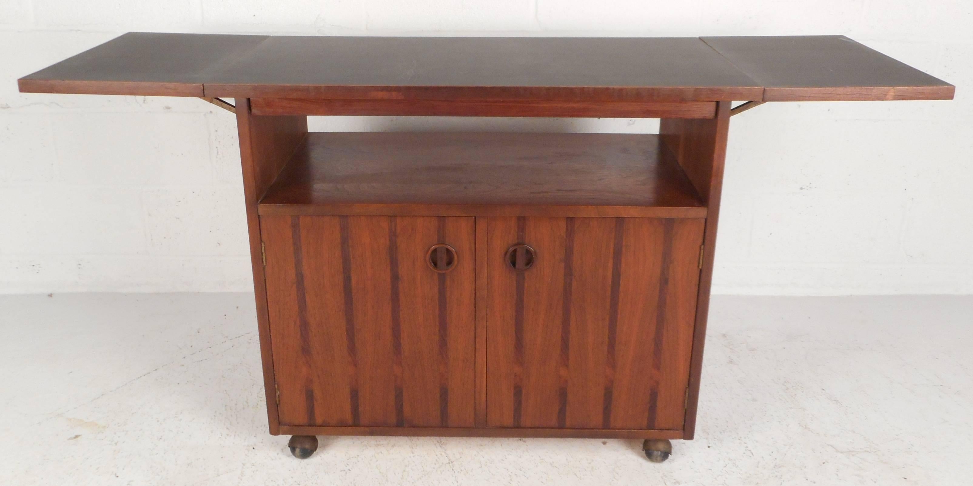 Stunning vintage modern walnut bar cart with unique rosewood striped accents, recessed circular pulls, and a pull-out Formica top tray. The sleek design has a drop-leaf Formica top that opens up to 60.25
