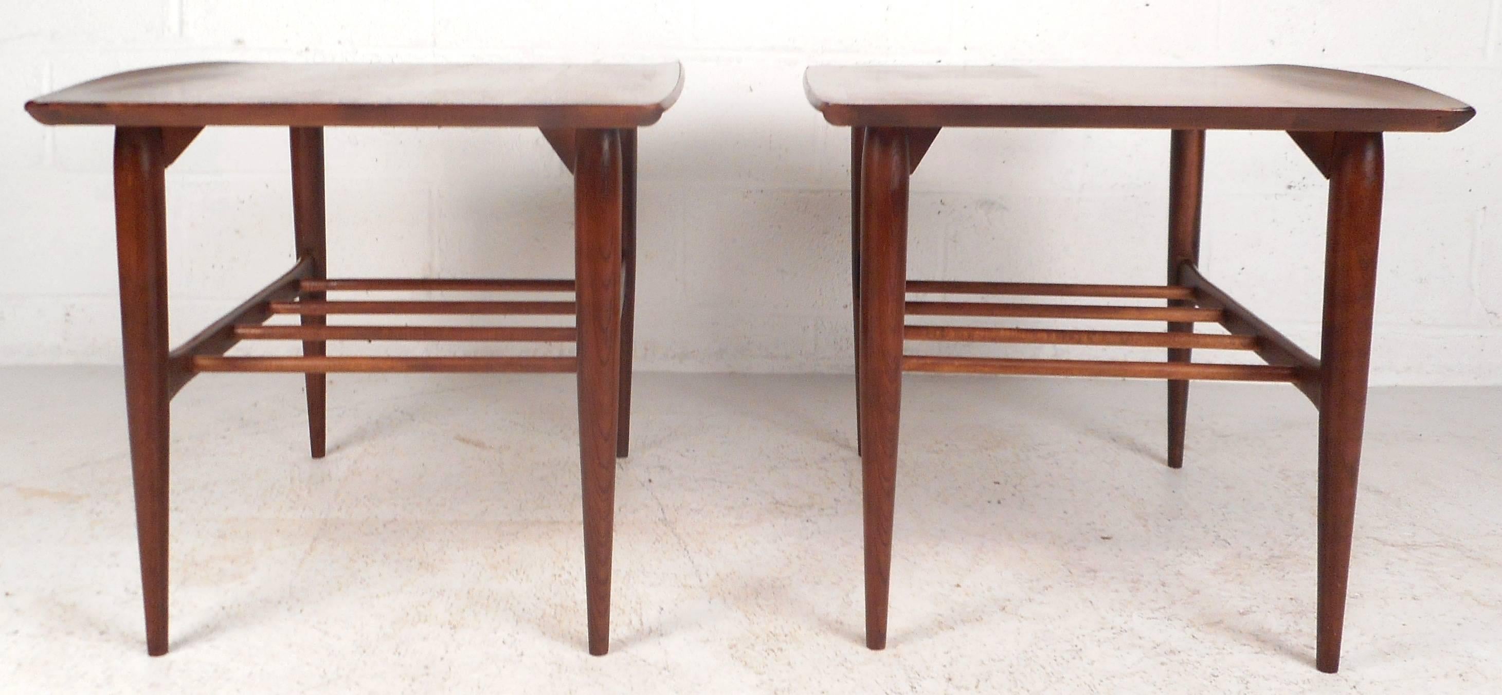 Impressive pair of vintage modern end tables feature unique raised edges, tapered legs, and a spoked second tier. Sculpted stretchers connect all four legs ensuring sturdiness without sacrificing style. Quality craftsmanship by Bassett Furniture