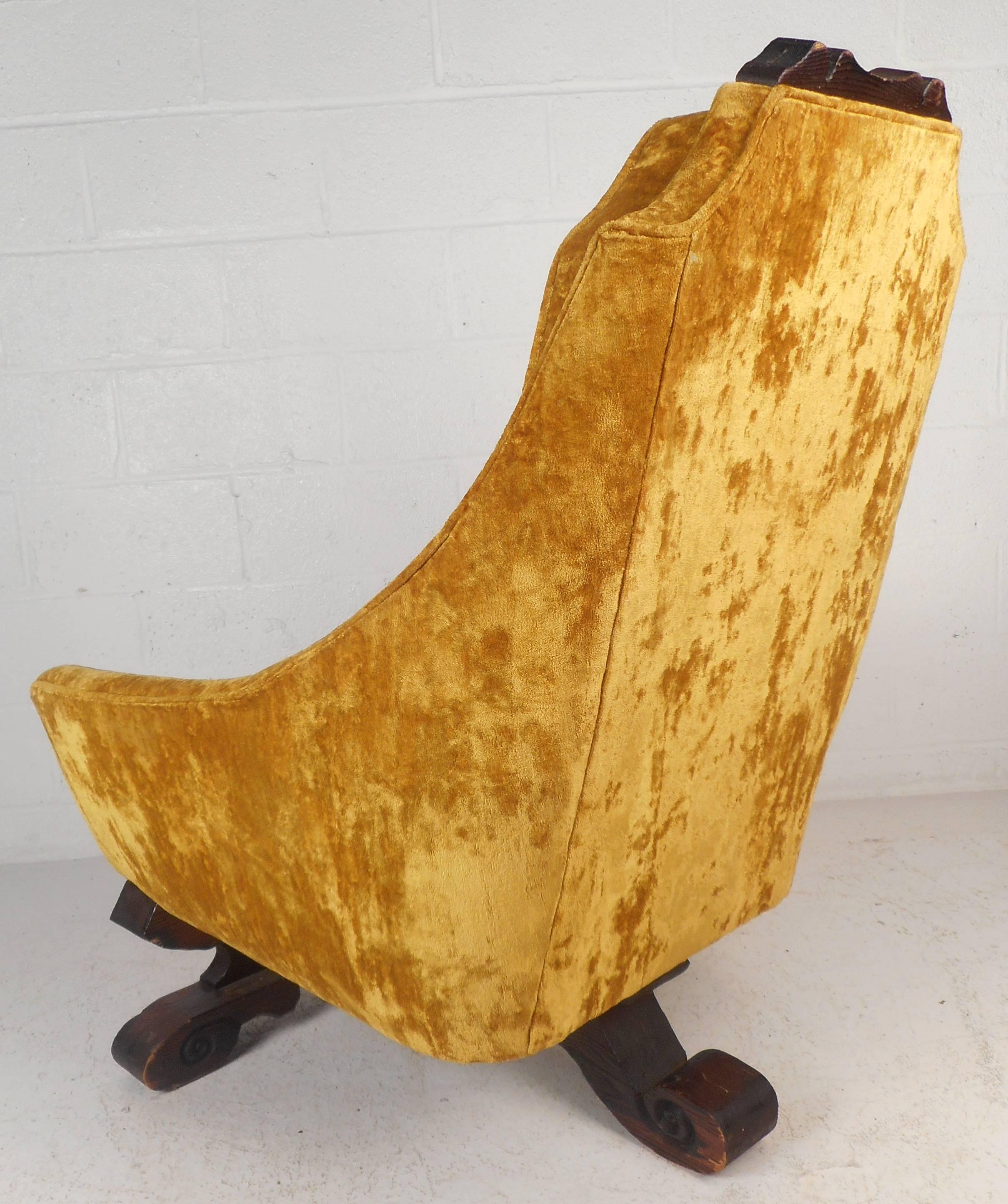 Impressive vintage modern lounge chair by Witco features a beautifully carved teakwood base with three legs and a carved top. The wide seat and high backrest are covered in plush yellow velvet upholstery. The detailed wood work and comfortable