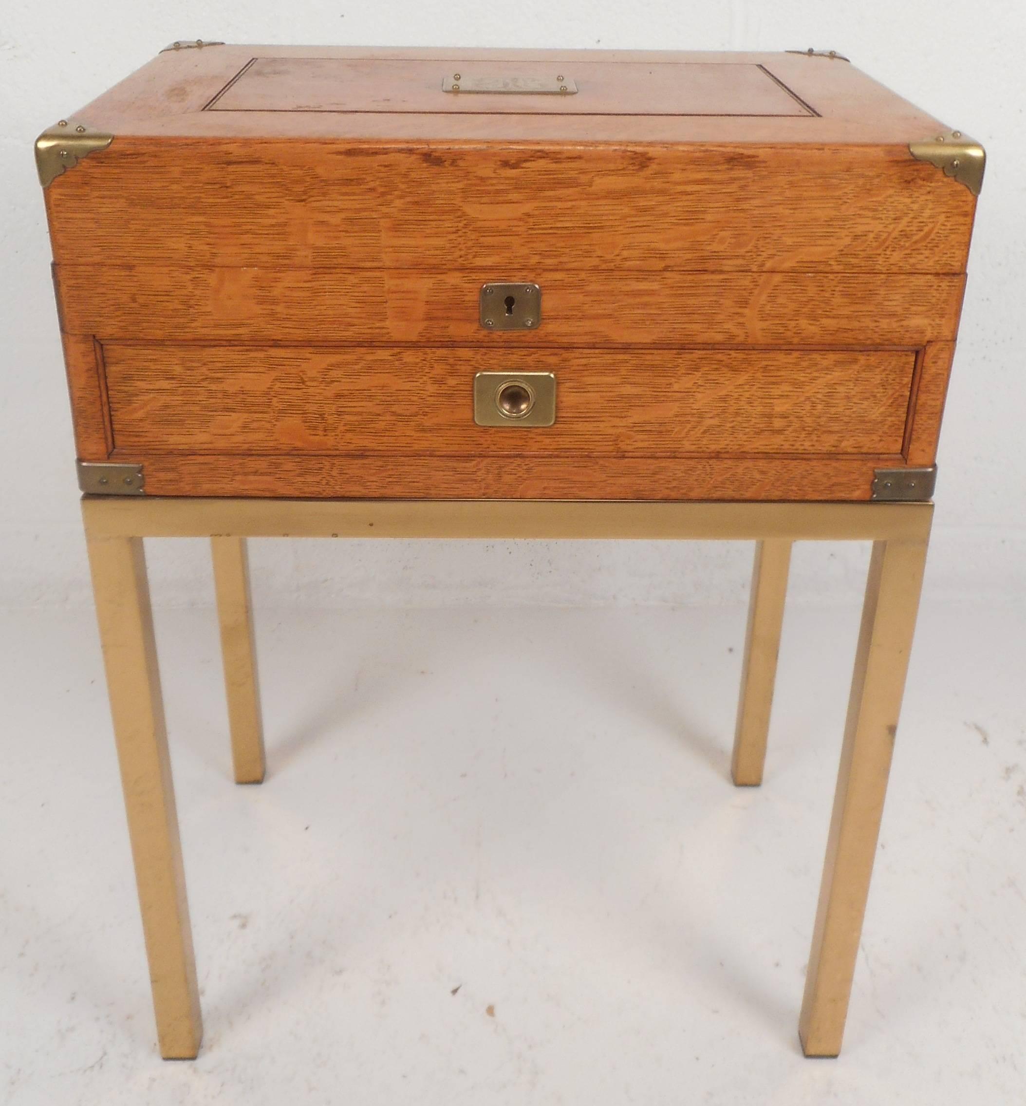 This elegant vintage modern Campaign style stand features intricate brass detail as well as four sturdy brass legs. Unique design has a single drawer and a lift up top for storage. This functional and stylish piece has sculpted handles on the sides