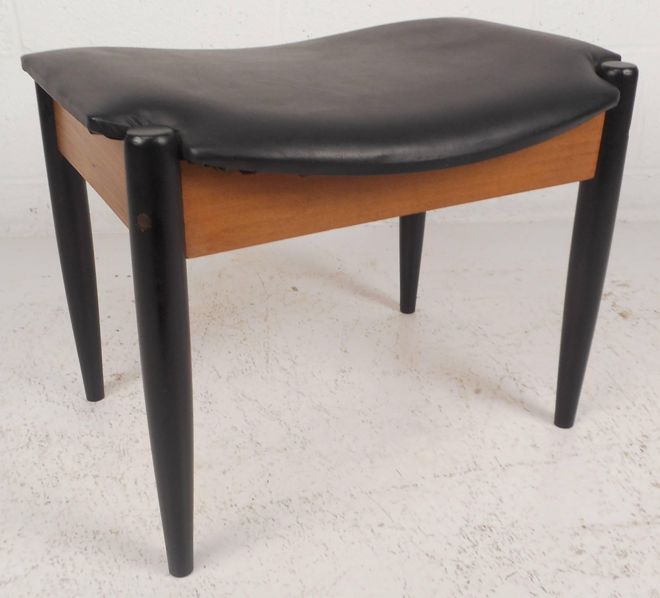 Elegant vintage modern foot stool features black lacquered legs. Unique walnut cross beams connect each leg adding sturdiness and style. The sleek black vinyl top is molded for comfort making this Mid-Century stool ottoman the perfect addition to