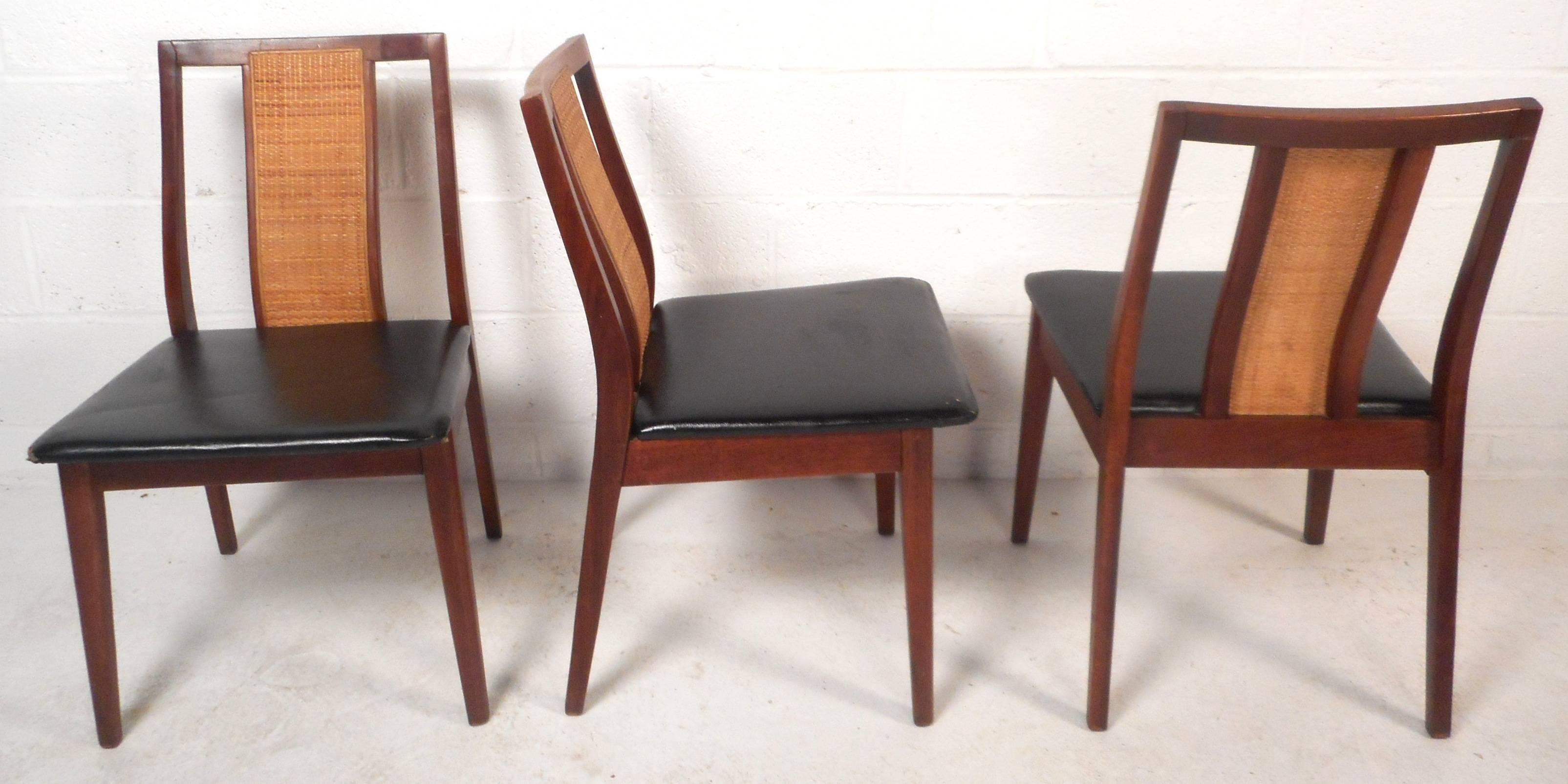 Elegant set of six vintage modern dining chairs feature solid walnut frames with black vinyl upholstery. Stylish design with cane in the center of the angled backrest and tapered legs. This sturdy and comfortable set of Mid-Century dining chairs