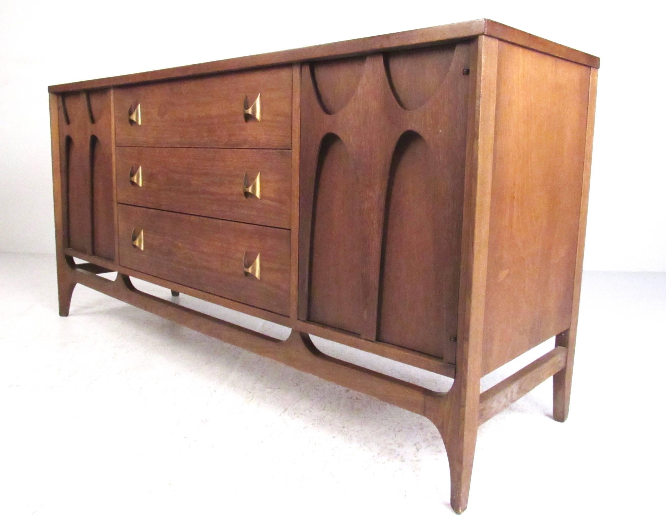 This uniquely sized walnut sideboard features classic Broyhill Brasilia sculpted cabinet doors and matching brass drawer pulls. This stylish mid-century sideboard makes a lovely addition to any interior and works well as a television console or
