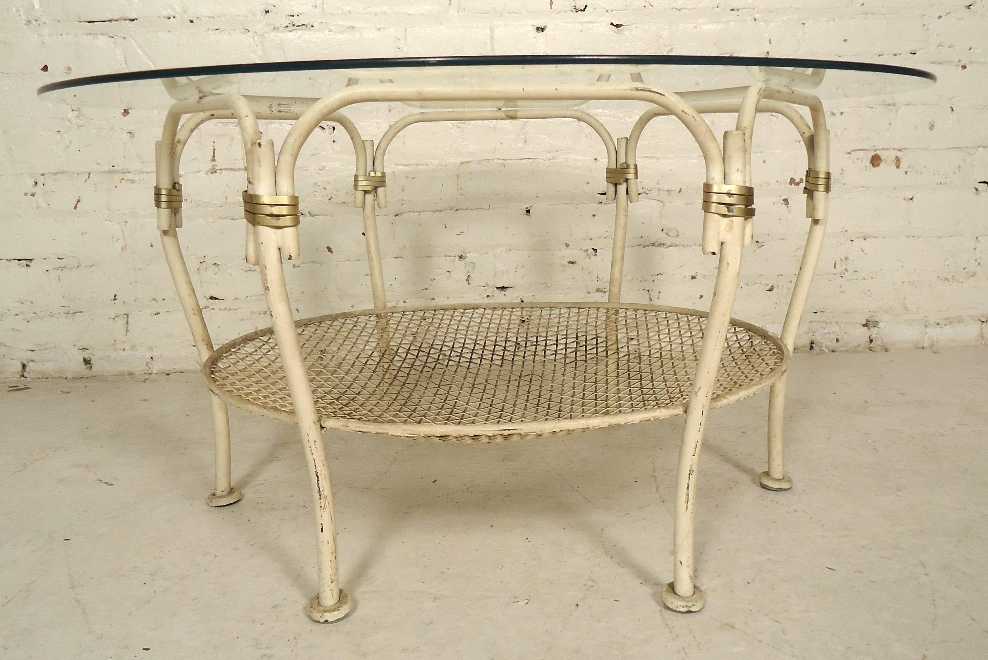 Unique style Mid-Century Modern round iron base table that can be used for an outdoor or indoor setting. Features a round glass top, brass colored ribbons, and a lower tier for storage.

(Please confirm item location NY or NJ with dealer).