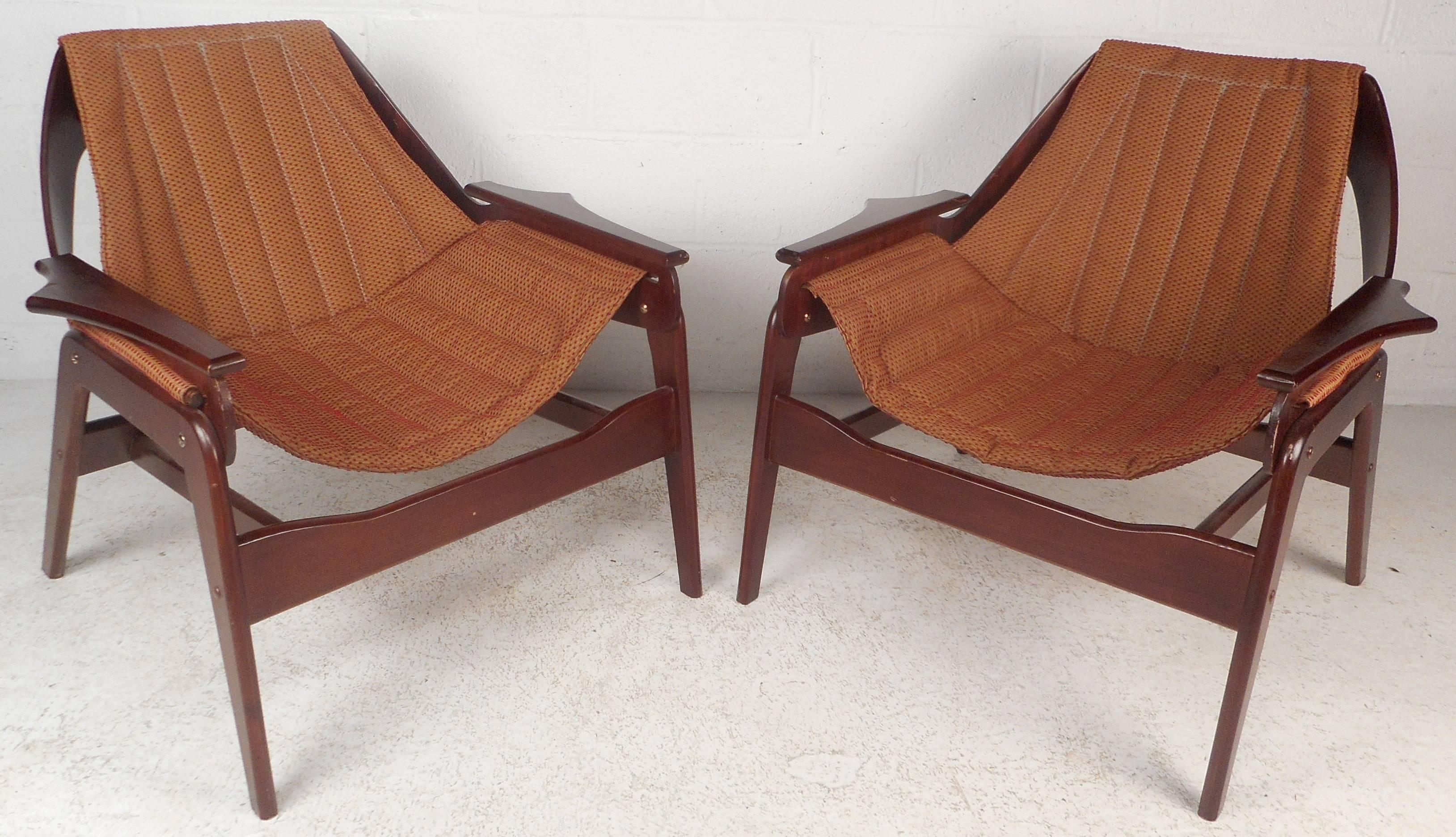 This stunning pair of vintage modern lounge chairs feature an upholstered sling design with a sturdy walnut frame. The sleek rounded backrest, angled legs, and unusual sculpted arm rests add to the allure. The unique construction offers comfort and