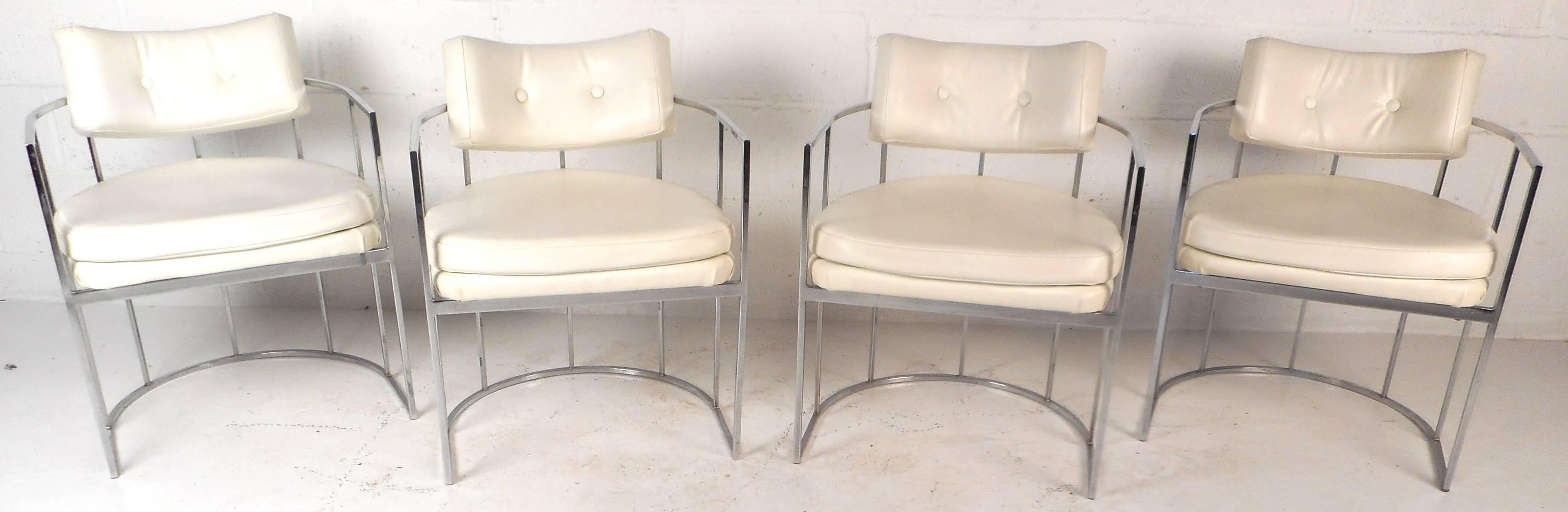 This elegant set of four vintage modern armchairs feature unique ellipse chrome frames that function as arm rests and a sturdy base. The sleek design is covered in white vinyl with thick padded seating and a tufted floating backrest. This stunning