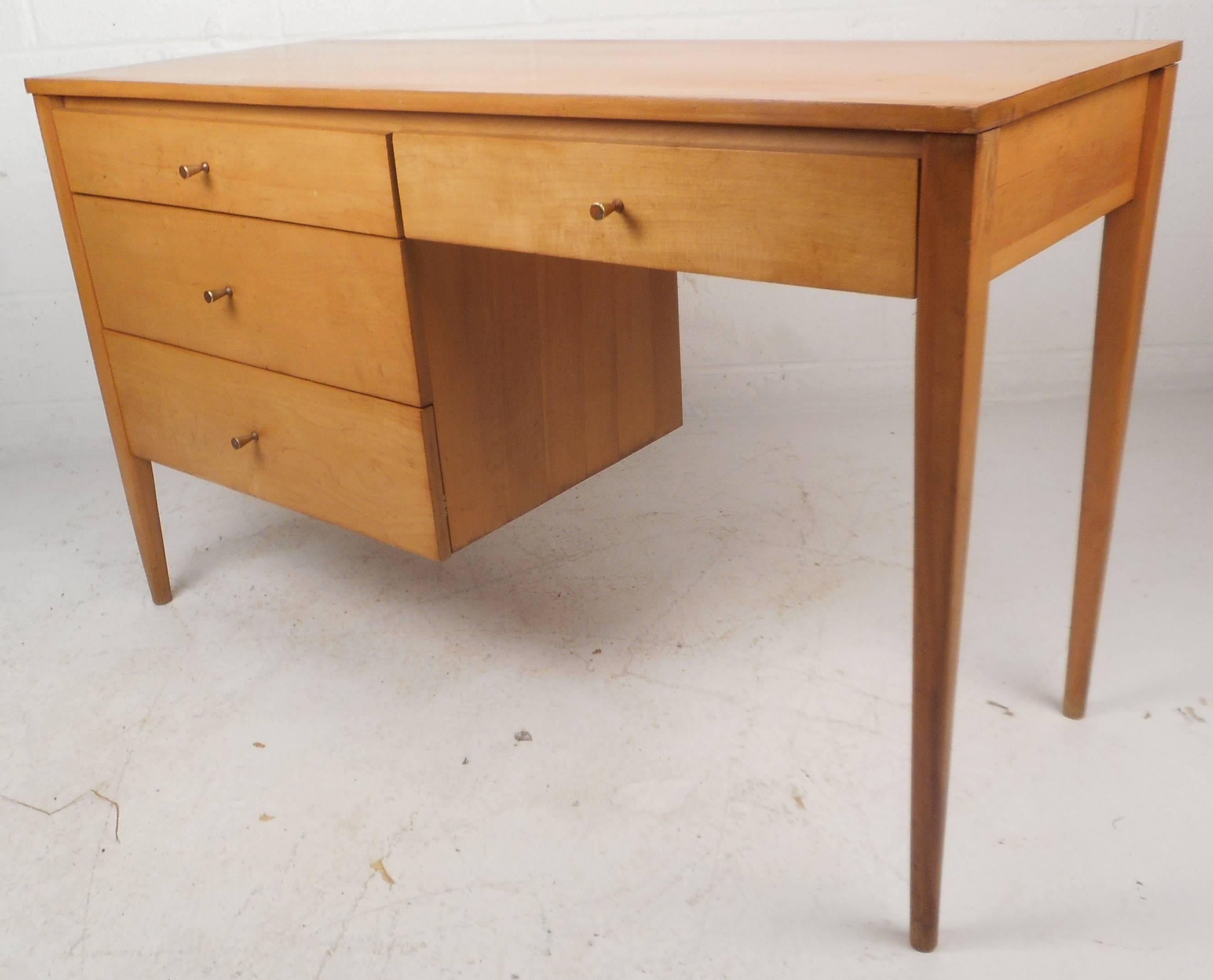 This stunning Mid-Century desk or vanity by Paul McCobb features a vintage maple finish with four drawers. Sleek design with unique cone shaped brass pulls and long tapered legs. This beautiful piece offers plenty of room for storage while providing