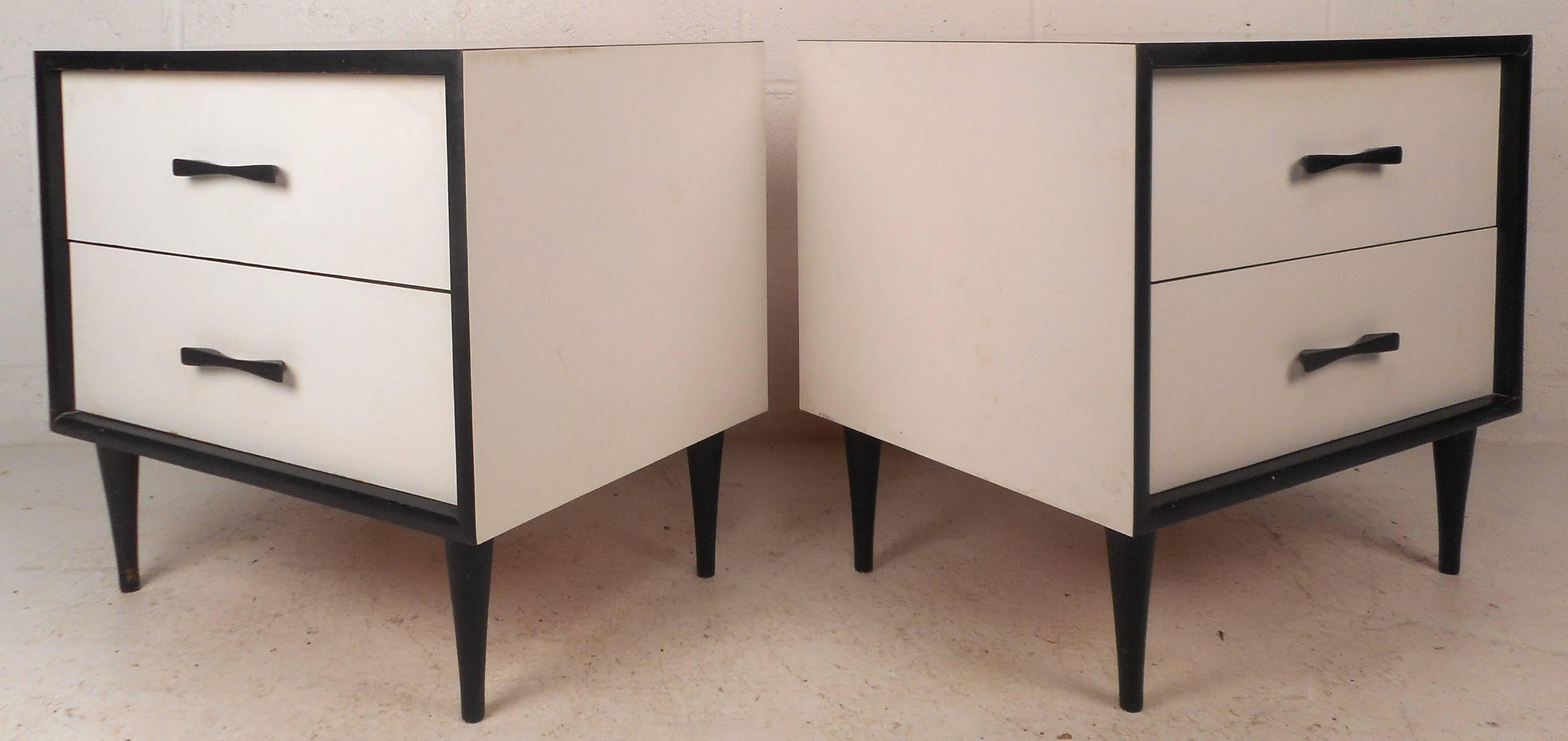 Elegant pair of vintage modern end tables feature unique black bow-tie pulls and tapered legs. Sleek design with white laminate and beautiful black trim around the fronts. Two hefty drawers offer plenty of room for storage without sacrificing style