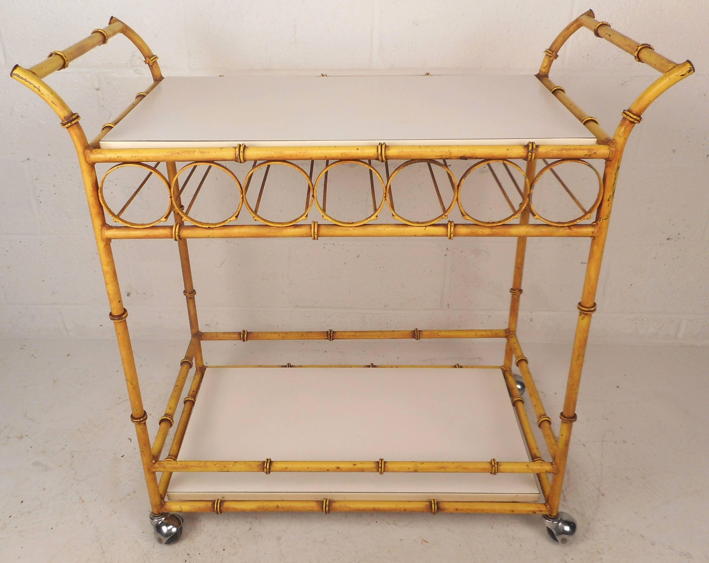 Beautiful vintage modern bar cart with two white laminate shelves and a yellow painted iron faux bamboo frame. Unique design features a smaller compartment underneath the top with thin rods. Gorgeous circular detail runs along each side making this
