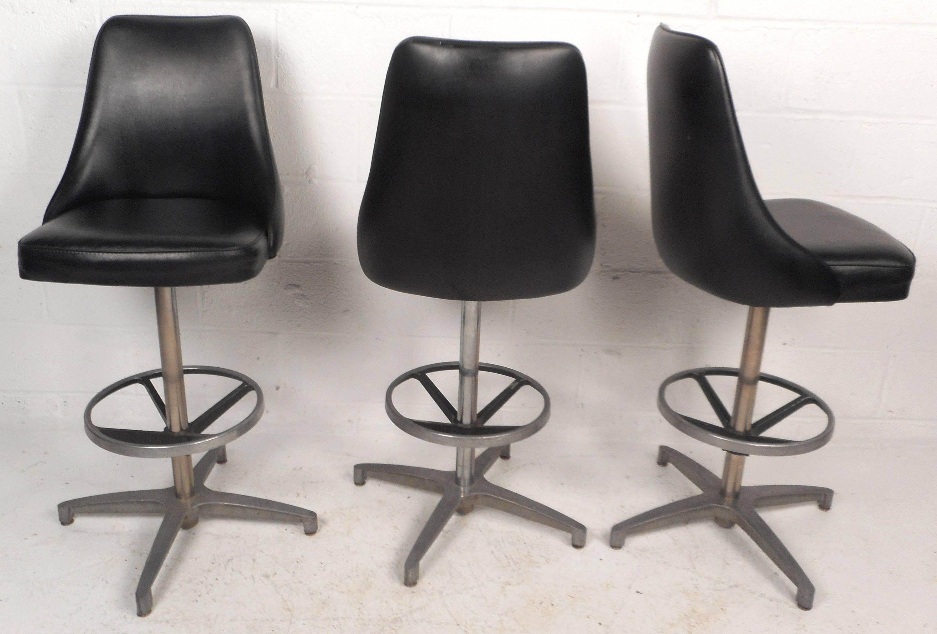 Stunning set of six vintage modern bar stools feature metal swivel bases with circular kick rest. Sleek design with black vinyl upholstery and comfortable bucket style seating. Stylish Mid-Century set makes the perfect addition to any seating