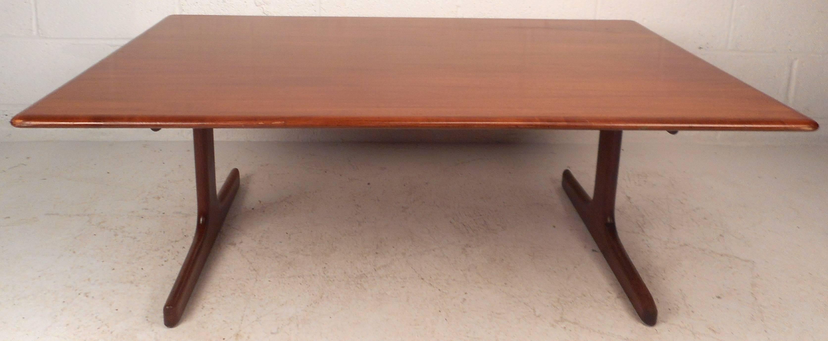 This gorgeous vintage modern coffee table features a unique base and smooth rounded edges along the top. The unusually large tabletop has beautiful teak wood grain adding to the allure. Quality construction ensures sturdiness and style in any modern