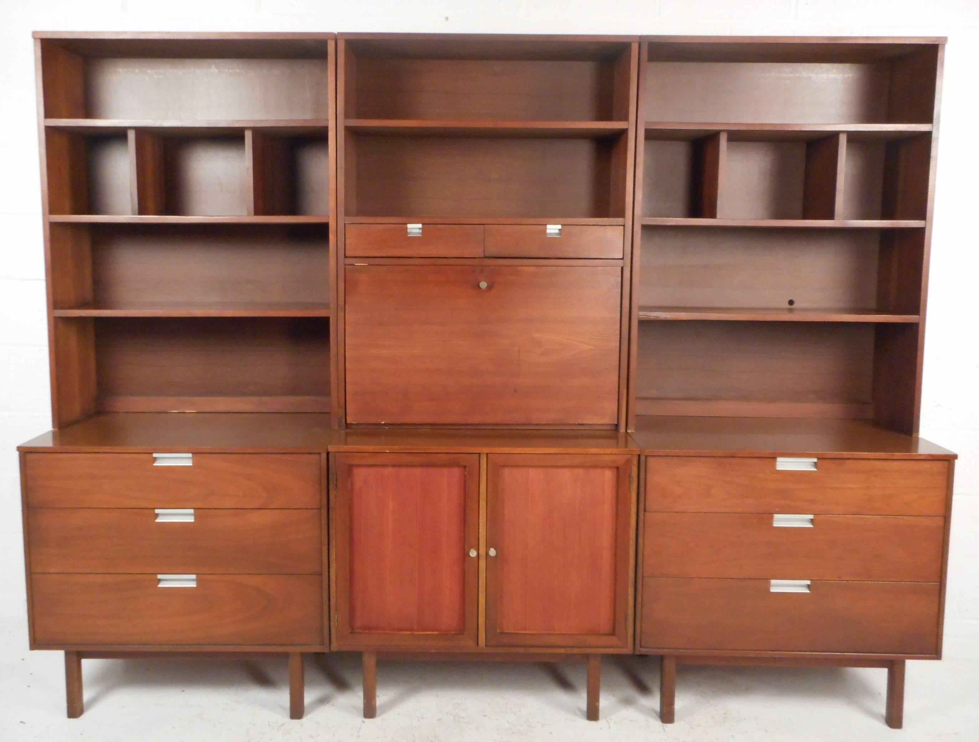 This impressive vintage modern wall unit features plenty of room for storage within its many drawers and compartments. Unique design with numerous shelves to put items on display as well as a drop front table and two cabinet doors. Sleek recessed