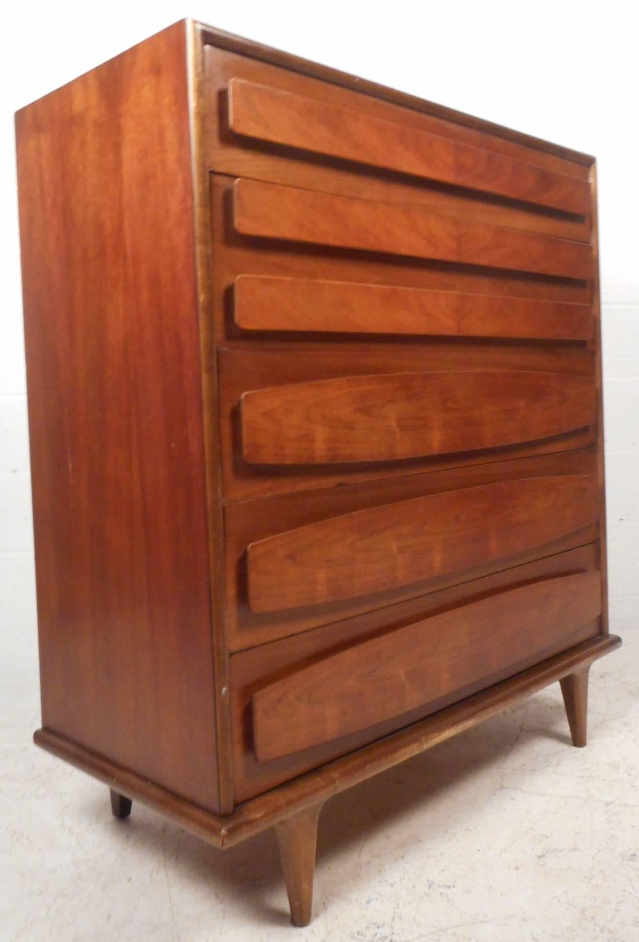 This stunning vintage modern dresser features unique embossed and sculpted drawer fronts that function as pulls. Sleek design with beautiful walnut wood grain and tapered legs. Dresser is made with true quality craftsmanship and offers plenty of