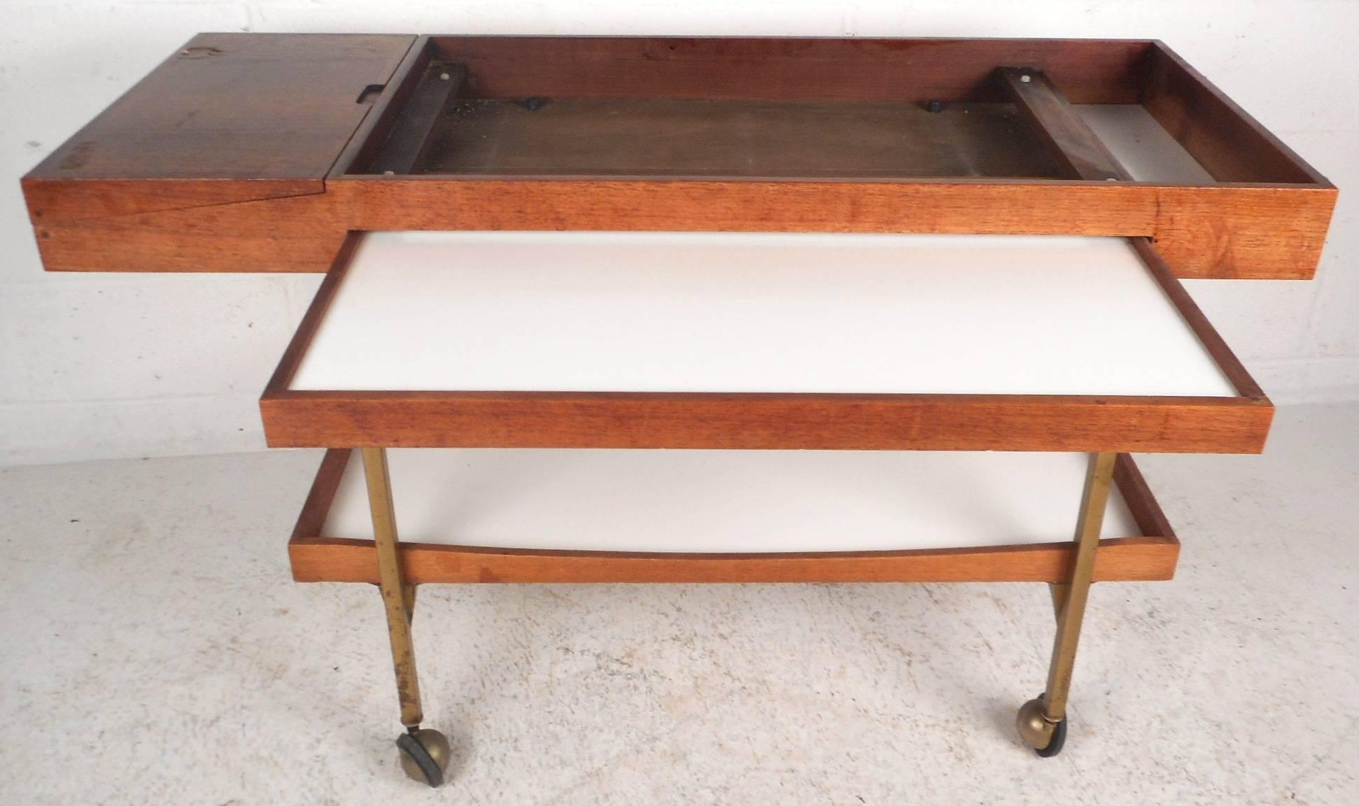 This stunning vintage serving cart features many hidden places to store and place items. Sleek design has a pull-out tray and a bottom tier with white laminate tops. Unique piece has a pull up side compartment that unveils another hidden area for