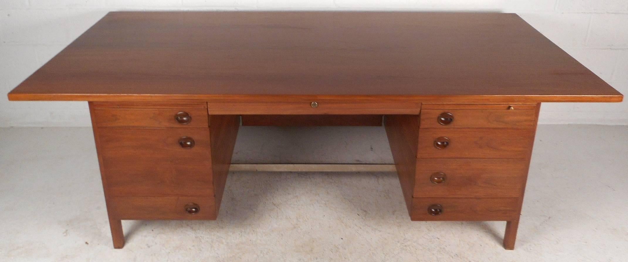 This beautiful vintage modern executive desk has an oversized work space with eight drawers and two pull out trays. Unique dark walnut recessed circular pulls, a metal stretcher, and a finished back show true quality craftsmanship. This elegant