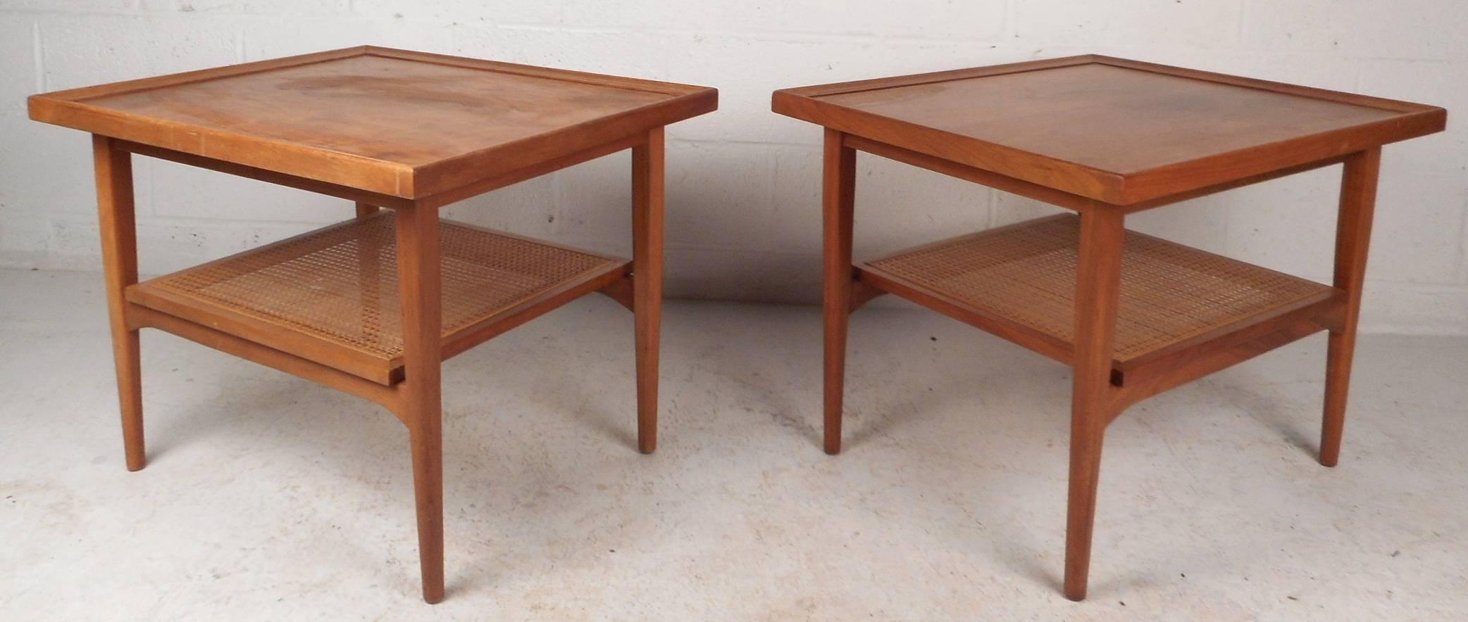 This gorgeous pair of vintage modern end tables feature a unique cane lower shelf for storing additional items. Quality construction with raised and bevelled edges along the tabletop. Stunning wood grain and tapered legs add to the allure. This