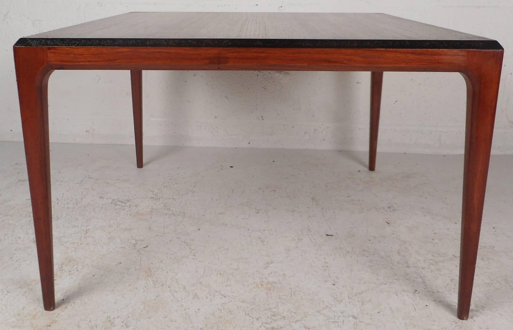 Beautiful vintage modern coffee table features stylish beveled edges with an ebonized strip that stretches all the way around the top. This sleek Mid-Century piece sits on top of four long and sturdy tapered legs. Versatile design with elegant