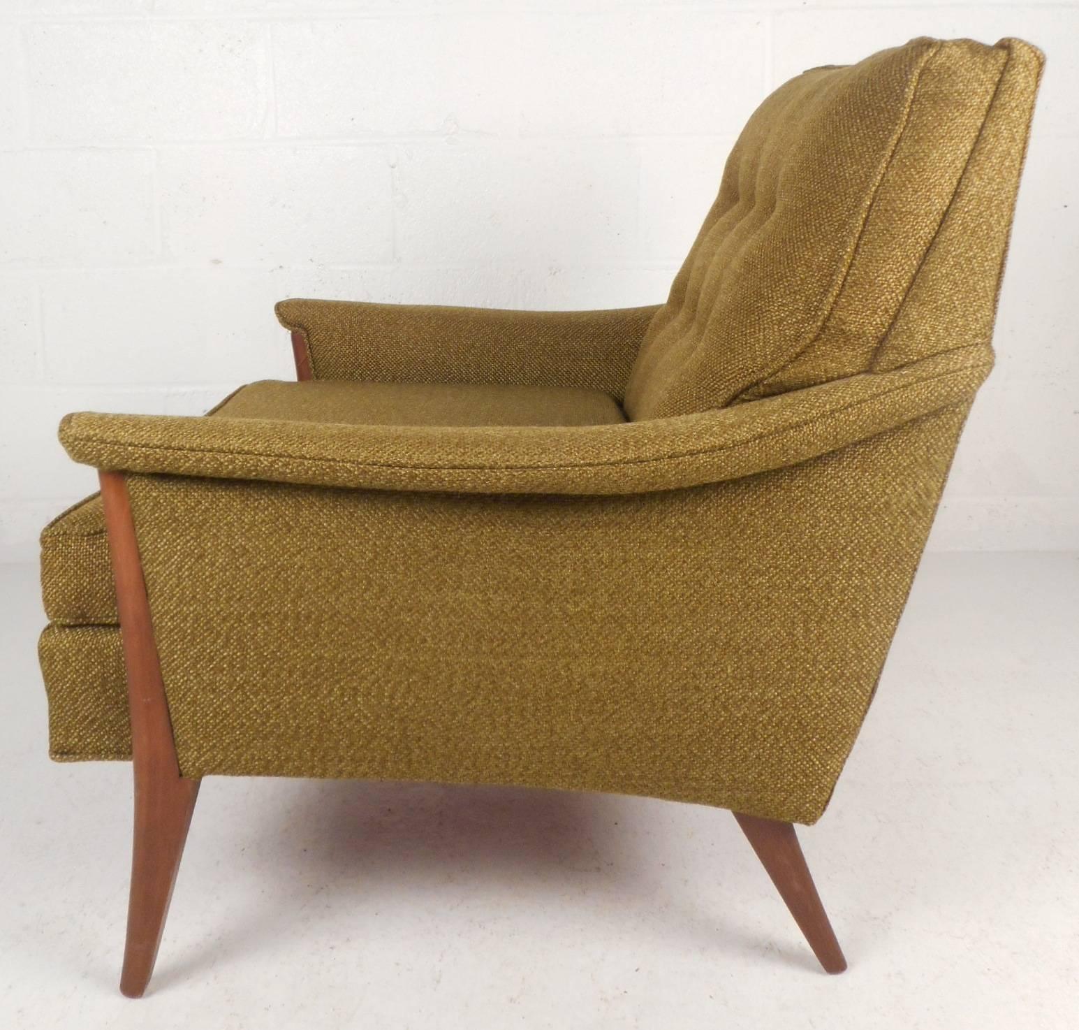 This stunning vintage modern lounge chair features a wide design with overstuffed cushions. Unique angled walnut legs and stylish winged arm rests add to the Mid-Century appeal. The elegant plush green upholstery and tufted backrest make this