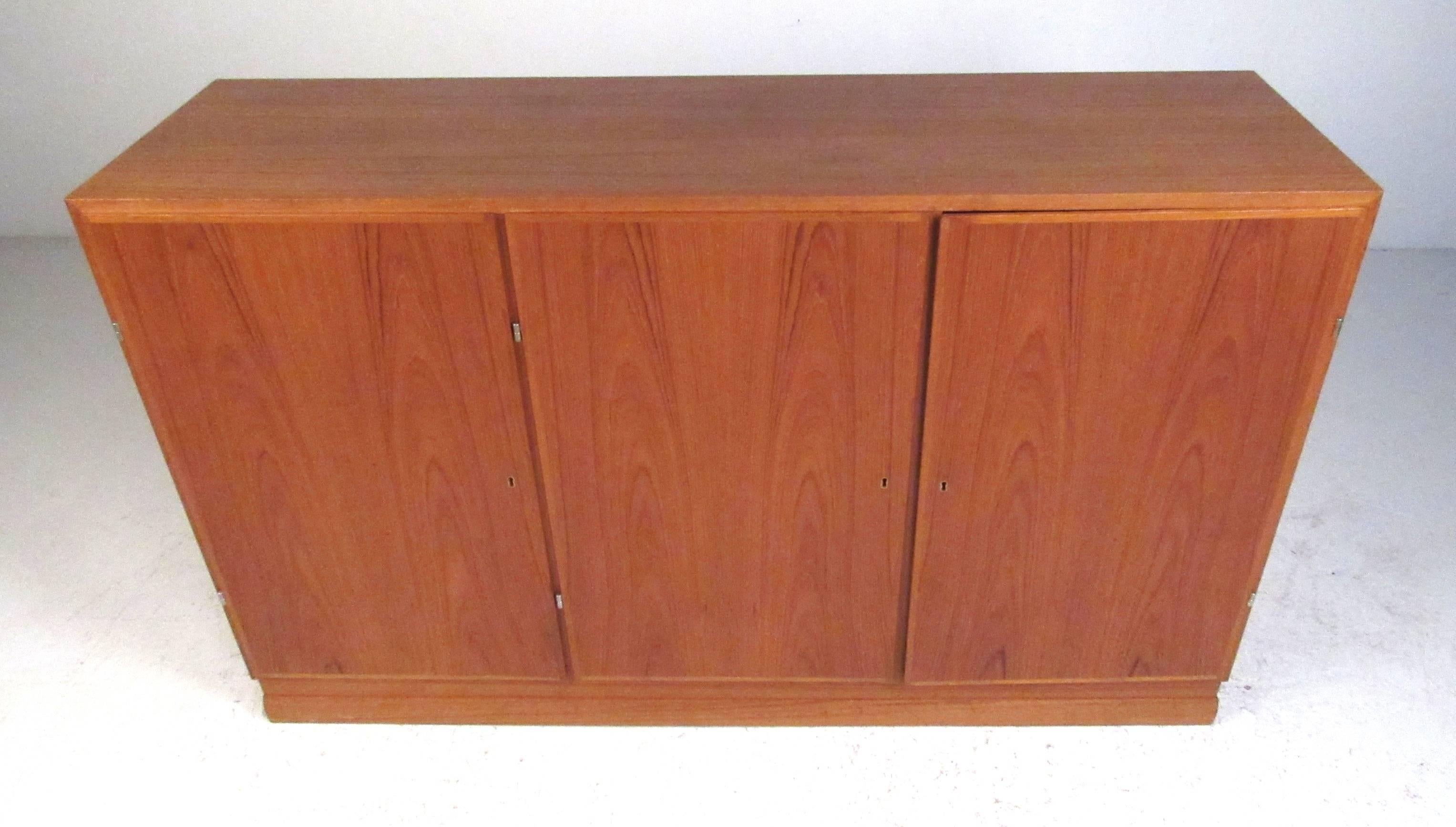 Armario moderno danés de tres puertas, de madera de teca, con interior de haya, compuesto por (10) estantes de almacenamiento y (4) bandejas forradas de fieltro. Por favor, confirme la ubicación del artículo (NY o NJ) con el distribuidor.