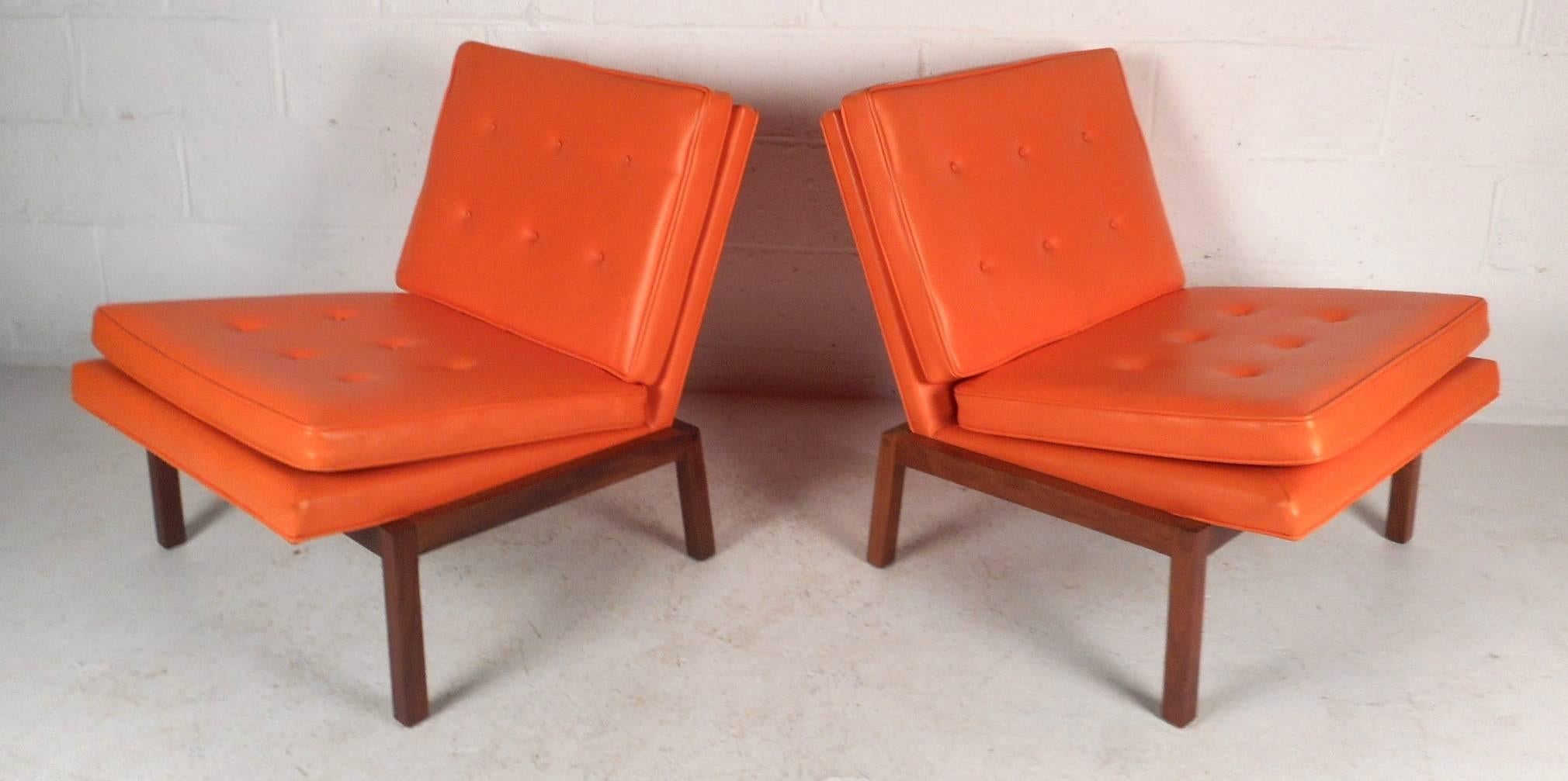Exquisite pair of vintage modern lounge chairs covered in elegant orange tufted vinyl. This stunning pair features a solid walnut base with angled legs and thick padded cushions. The unique wide design has smaller rear legs so that this piece leans